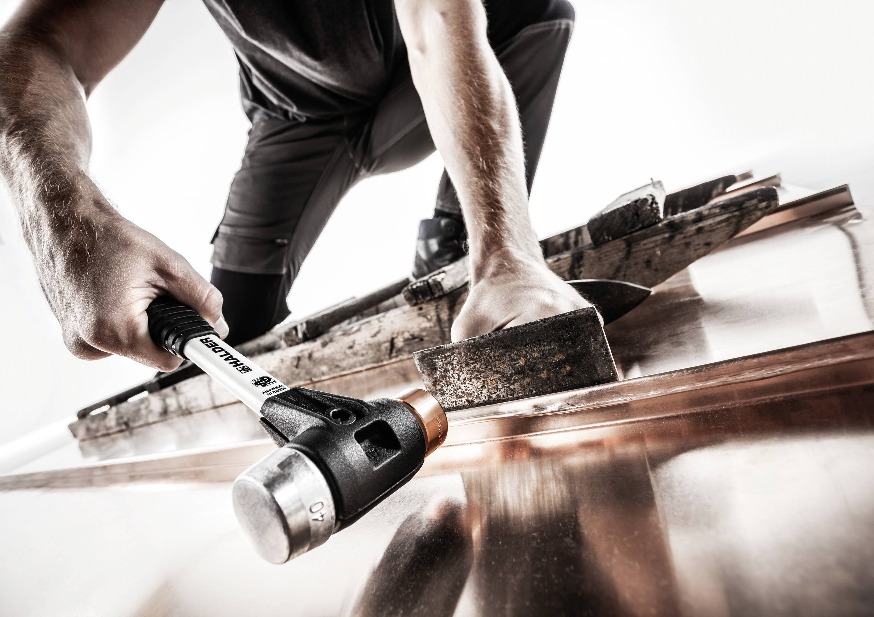Ein Handwerker bearbeitet ein Kupferblech mit einem Hammer und einer Holzplatte. Die Szene betont handwerkliches Geschick und Präzision.
