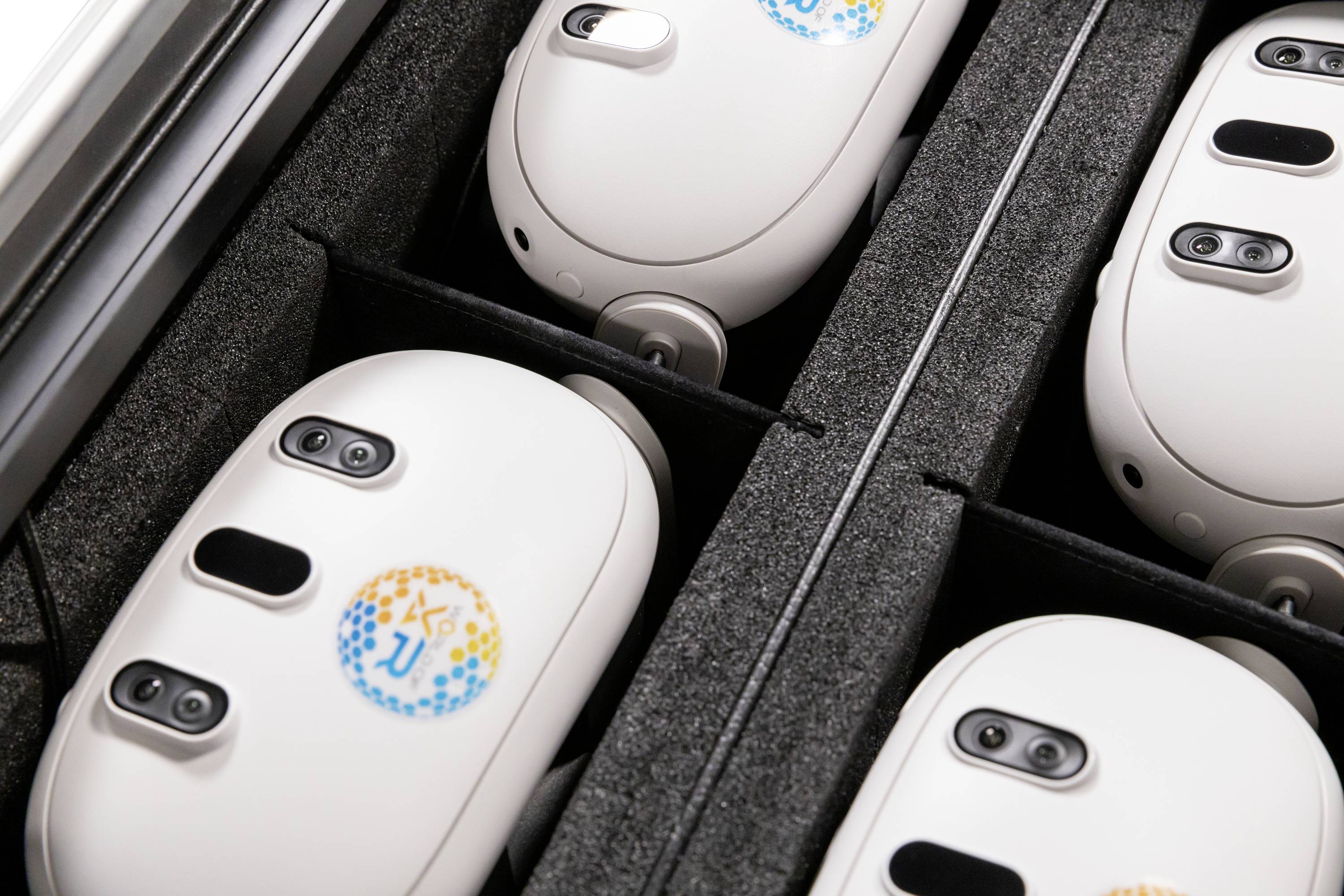 Vier weiße, ovale Geräte mit Kameras und bunten Aufklebern liegen in einem Schaumstoffetui.