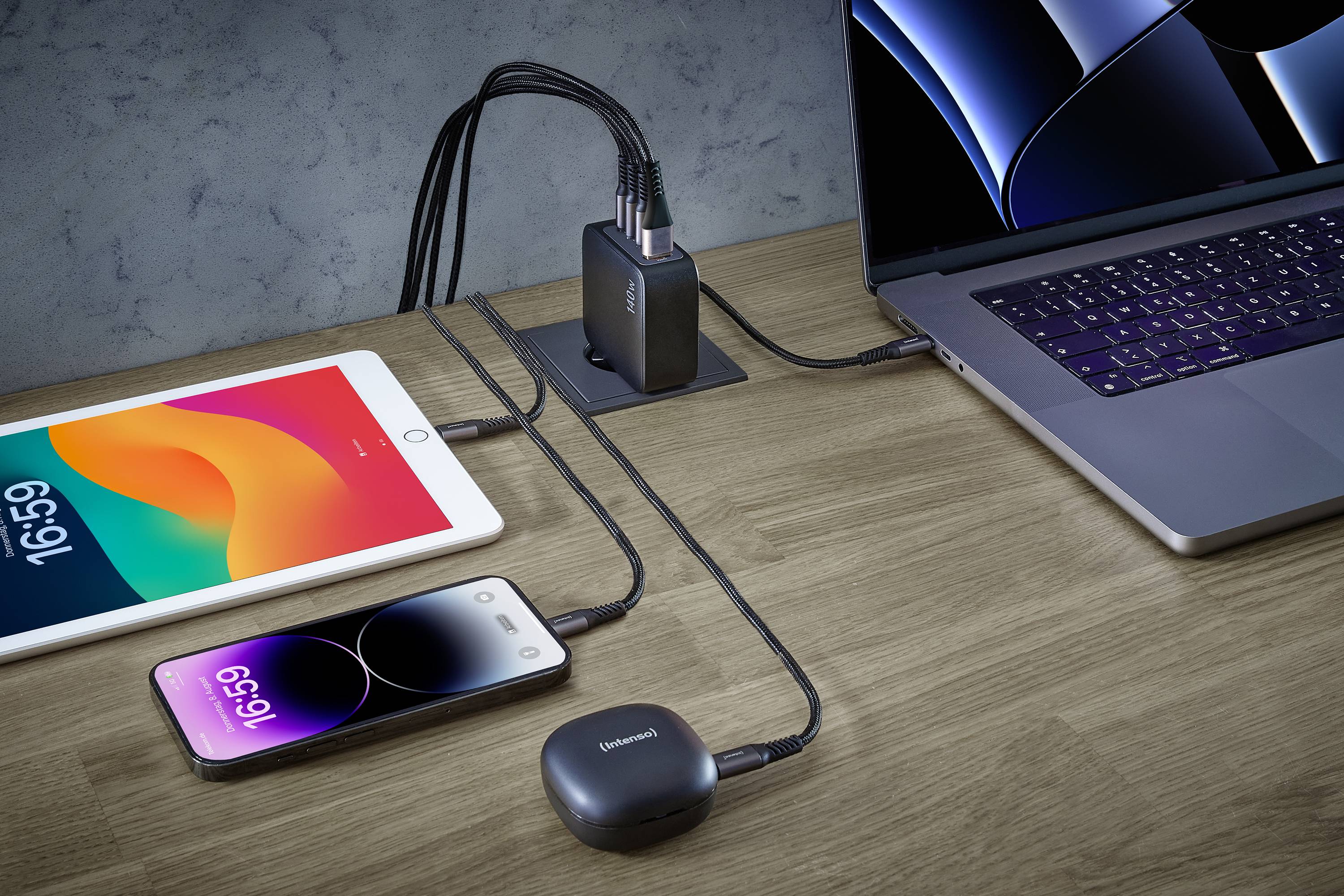 Ein Tablet, zwei Smartphones und ein Laptop sind an einen USB-Ladeadapter angeschlossen, der auf einem Holztisch steht.