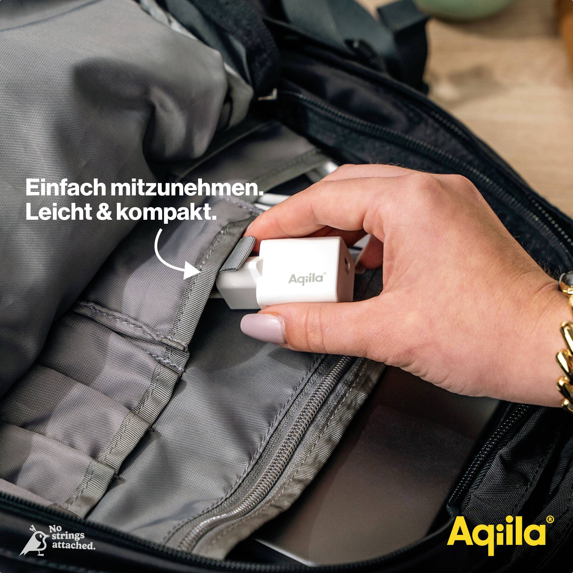Eine Person legt einen kleinen, weißen Reiseadapter mit dem Aufdruck 'Aqiila' in eine Tasche. Text sagt: 'Einfach mitzunehmen. Leicht & kompakt.'