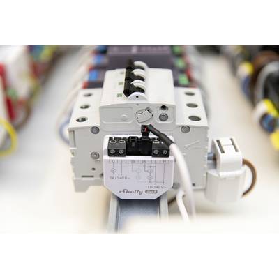 Ein elektrisches Relais mit Beschriftung 'Shelly 2.4/240V' ist auf einer DIN-Schiene montiert, umgeben von farbigen Kabeln.