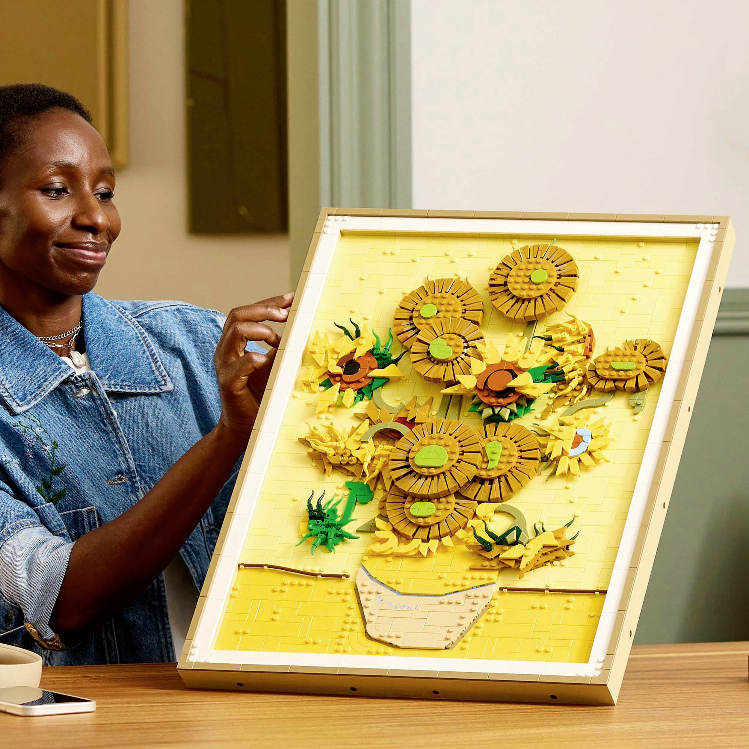 Eine Person betrachtet ein Kunstwerk aus LEGO-Steinen, das einen Strauß Sonnenblumen in einem Korb darstellt.