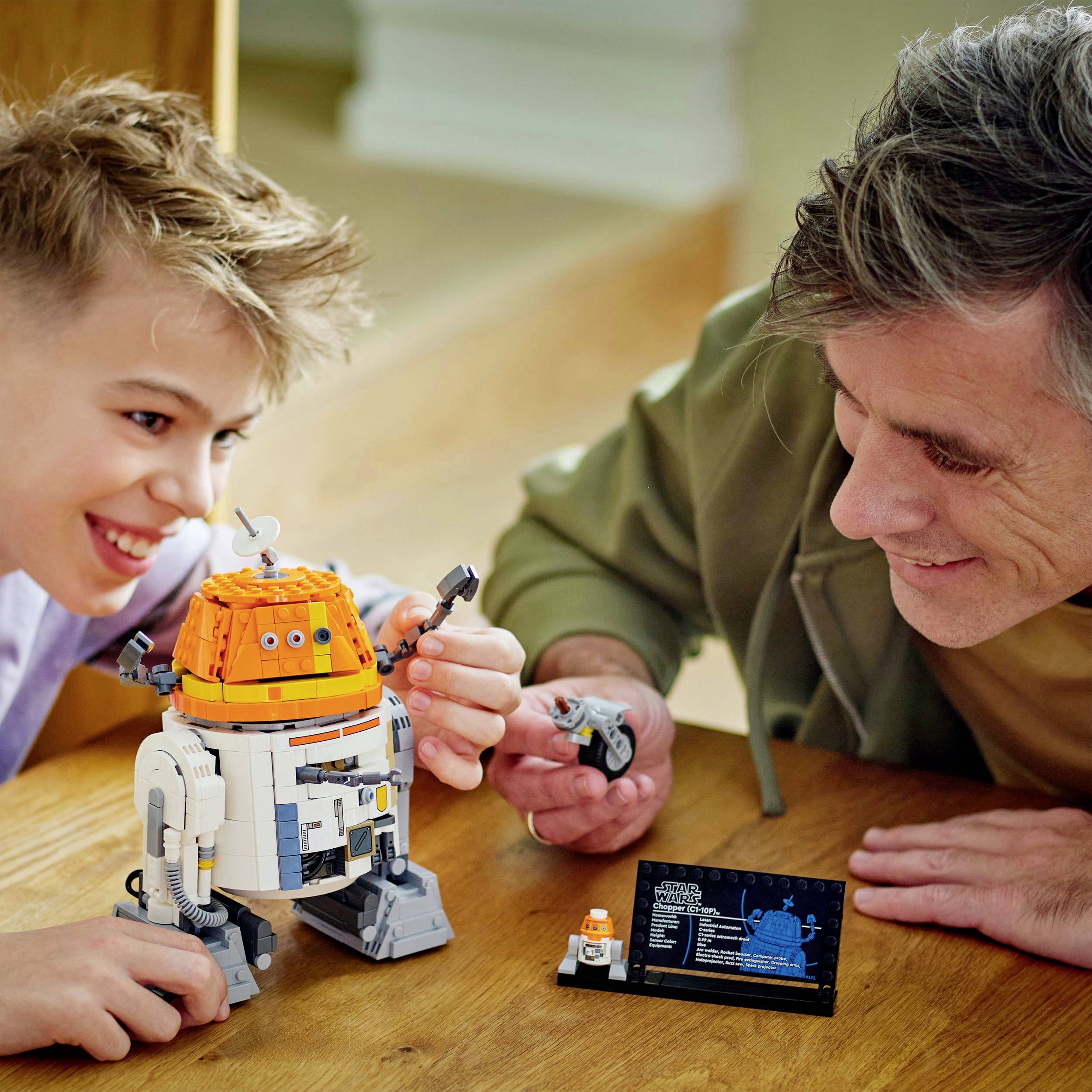 Ein Kind und ein Erwachsener bauen und betrachten gemeinsam ein Modell eines Roboters. Beide wirken glücklich und konzentriert.