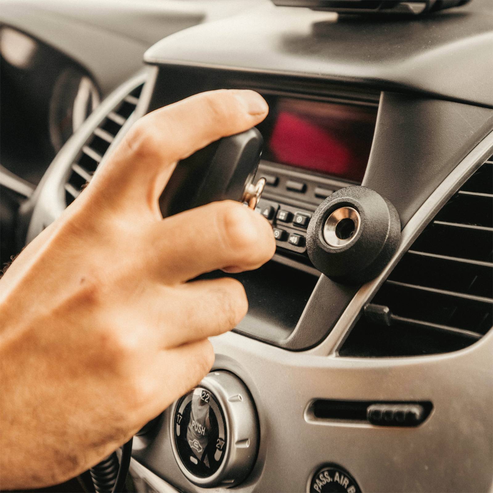 Eine Hand hält einen Autoschlüssel vor ein Armaturenbrett mit einem Zündschloss. Das Auto-Entertainment-System ist im Hintergrund sichtbar.