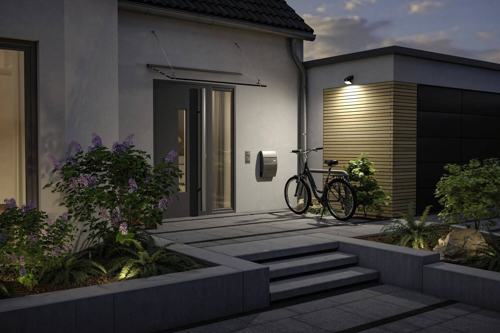 Ein modernes Haus mit Vordergarten bei Dämmerung. Eine Fahrrad steht neben der Eingangstür, beleuchtet von warmem Außenlicht.