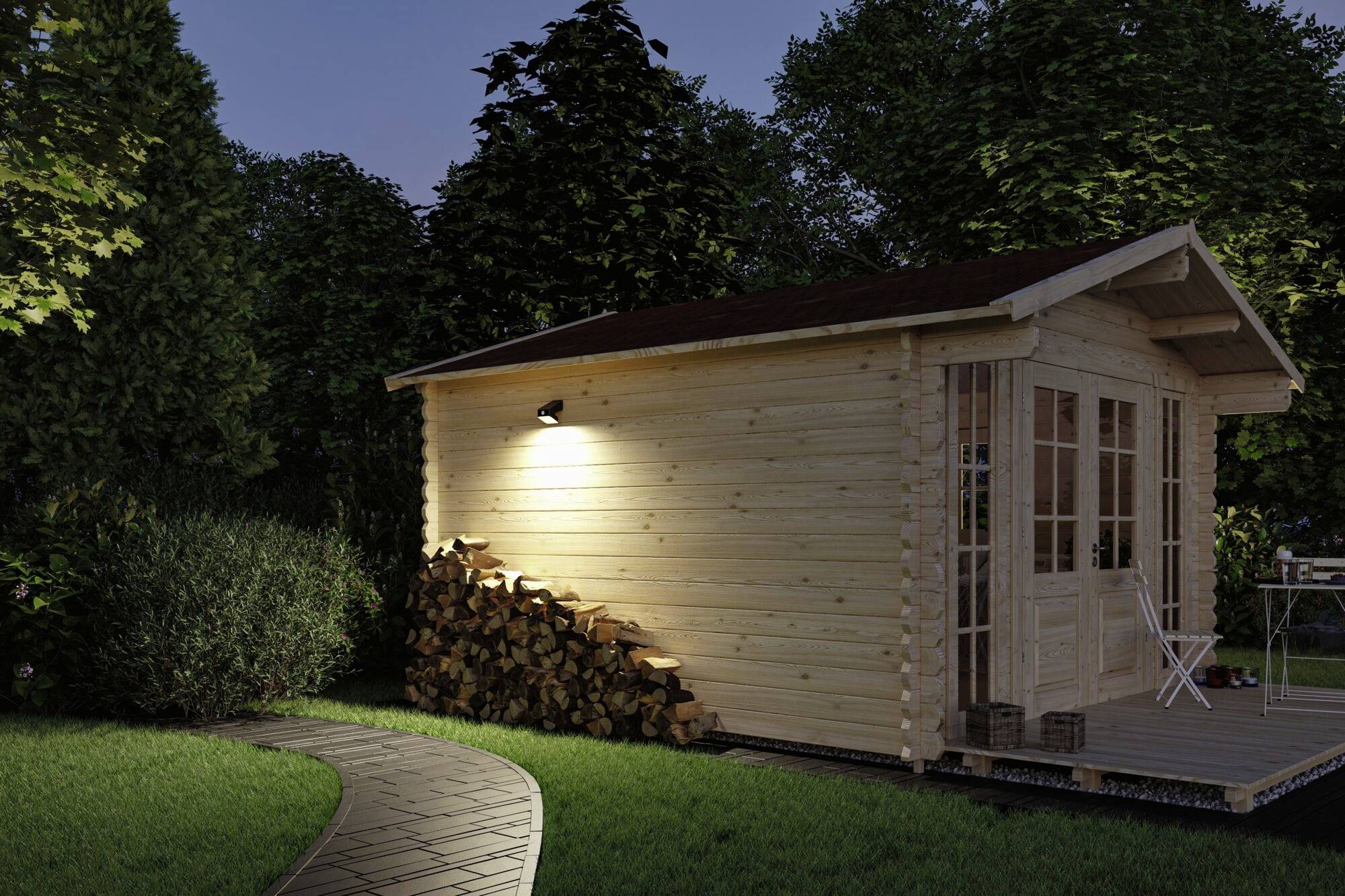 Holzhütte im Garten bei Nacht, mit Stapel Brennholz daneben und einem gepflasterten Weg, der im Vordergrund verläuft. Beleuchtung außen an der Hütte.