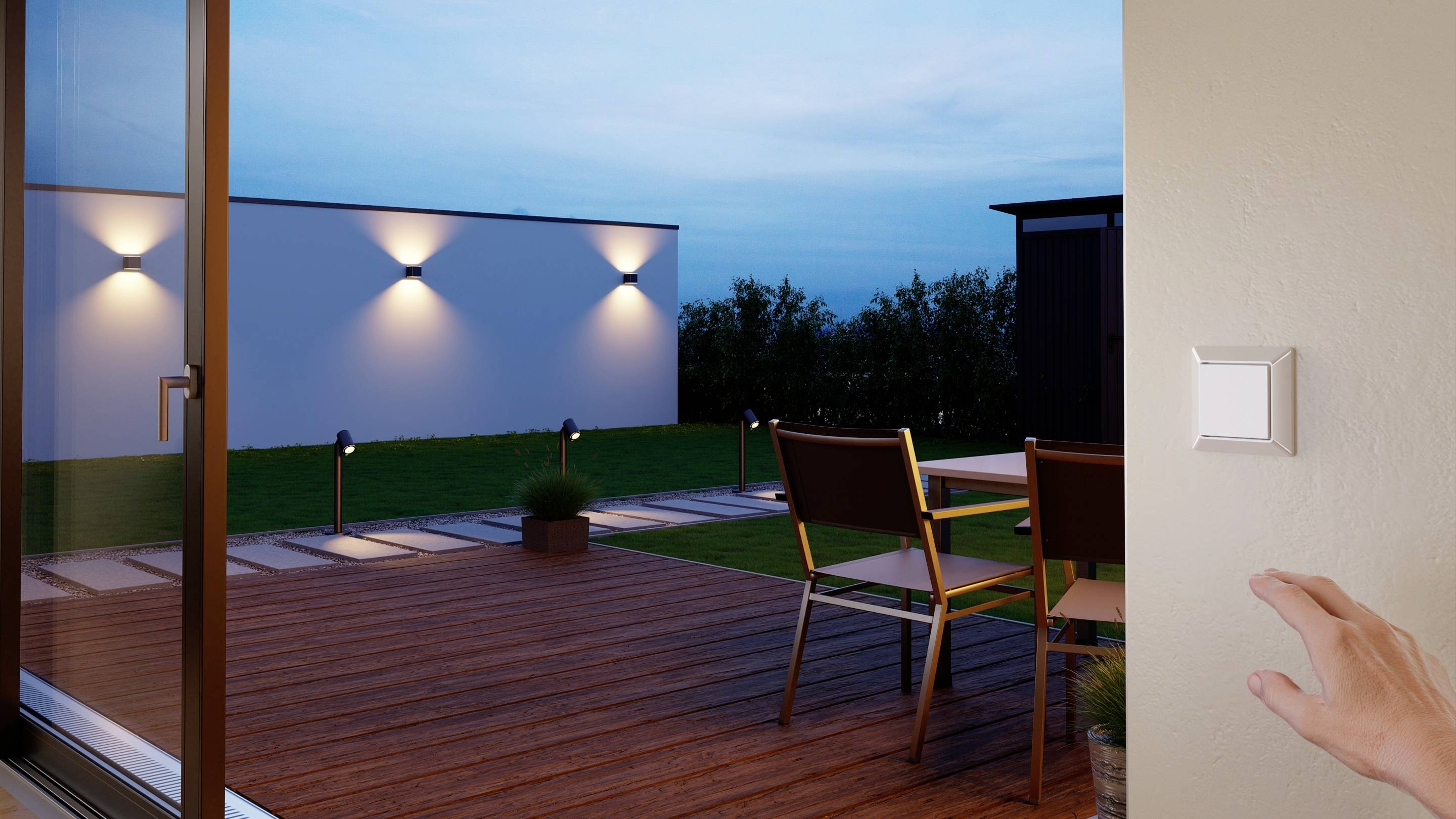 Eine Hand betätigt einen Lichtschalter, während draußen auf der Terrasse modernes Außenlicht leuchtet.