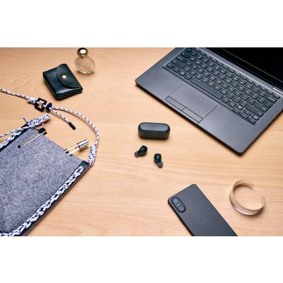 Ein Laptop, ein Smartphone, kabellose Ohrhörer und Zubehör auf einem Holztisch. Alltagstechnologie und Gadgets für mobiles Arbeiten.