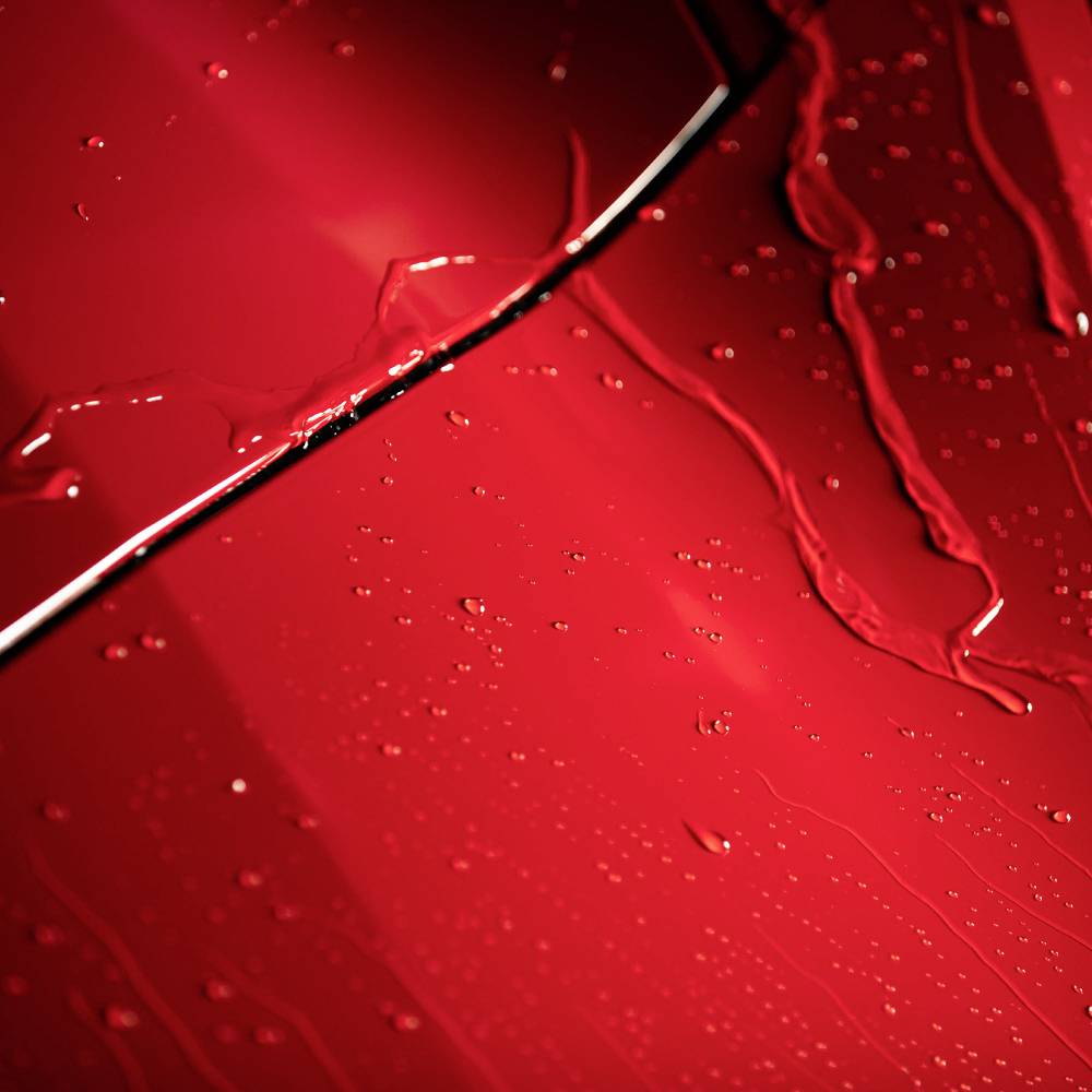 Rotes Autooberfläche mit Wassertropfen, die reflektiertes Licht erzeugen, was eine glänzende und dynamische Textur darstellt.