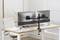 Zwei Monitore auf einem Schreibtisch, befestigt an einem Dual-Monitor-Arm. Im Hintergrund ist ein Bürostuhl und ein Bild an der Wand.