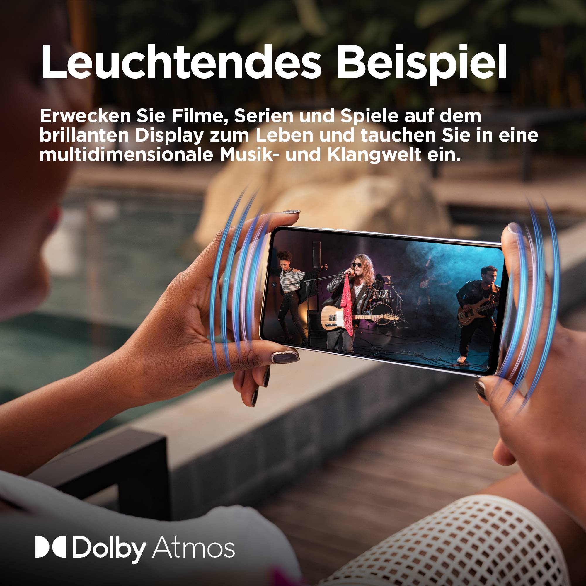 Hand hält Handy mit Konzertvideo, blaue Klangwellen hervorgehoben. Text: 'Leuchtendes Beispiel', beschreibt eindringliche Dolby Atmos Erfahrung.