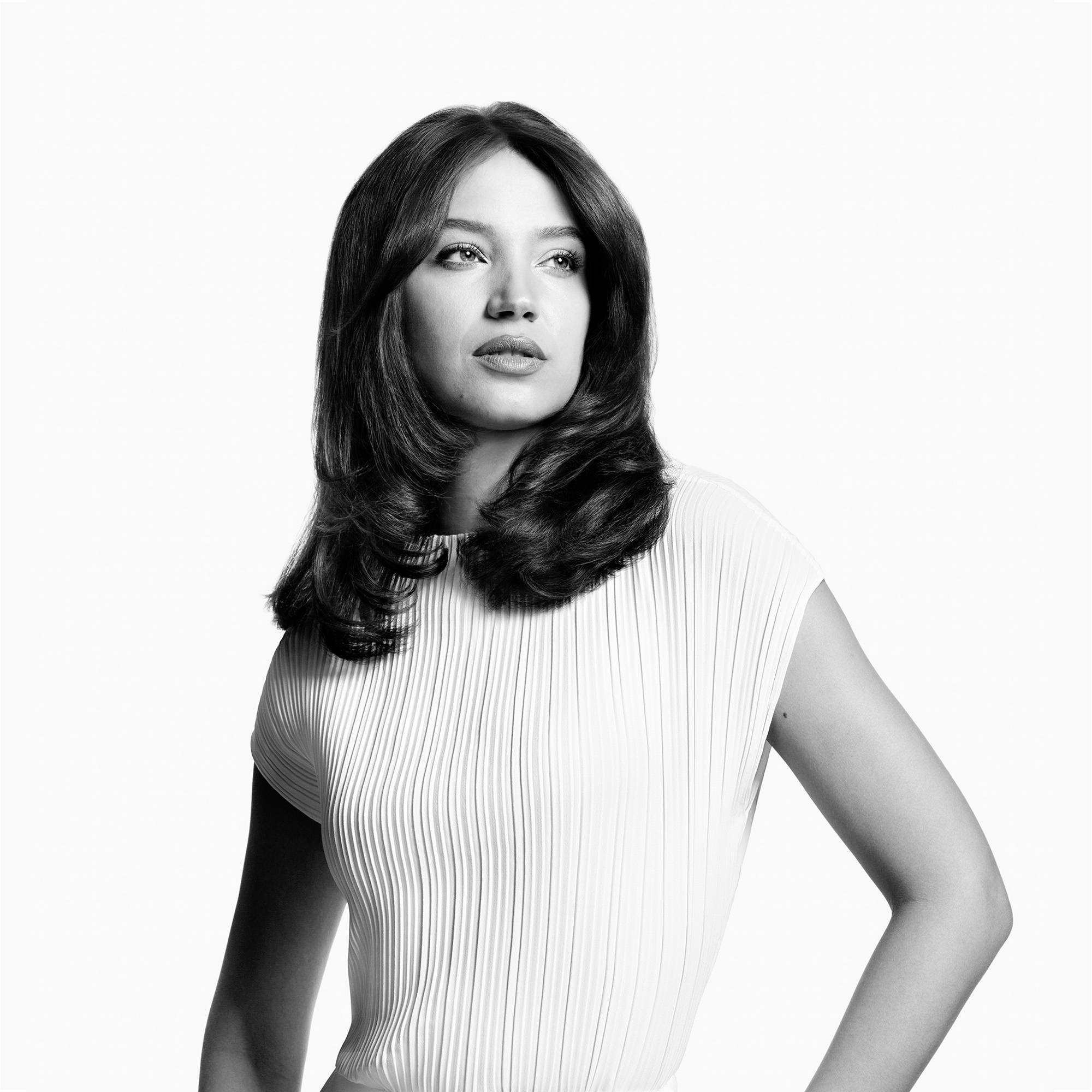 Frau mit welligem Haar und weißem Kleid, schaut zur Seite. Elegantes, zeitloses Porträt in Schwarz-Weiß.