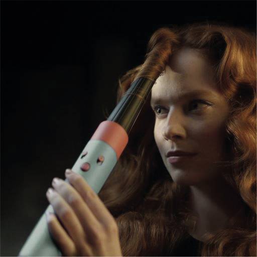 Frau mit rotem Haar verwendet einen Lockenstab zum Stylen ihrer Haare. Sie konzentriert sich auf das Gerät in ihrer Hand.