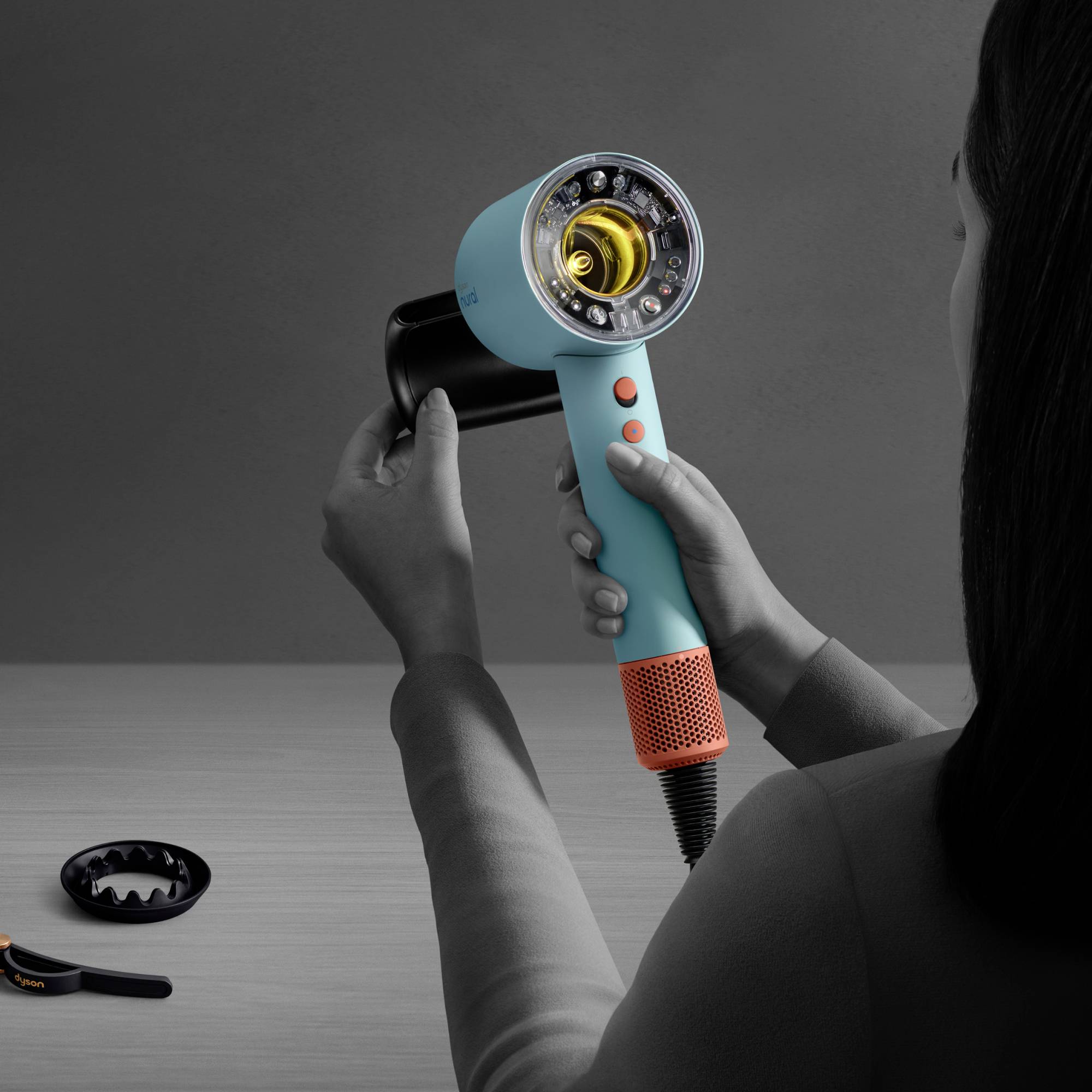 Eine Person hält einen modernen Haartrockner mit sichtbarem Innenleben über einem Tisch. Zubehörteile liegen daneben.