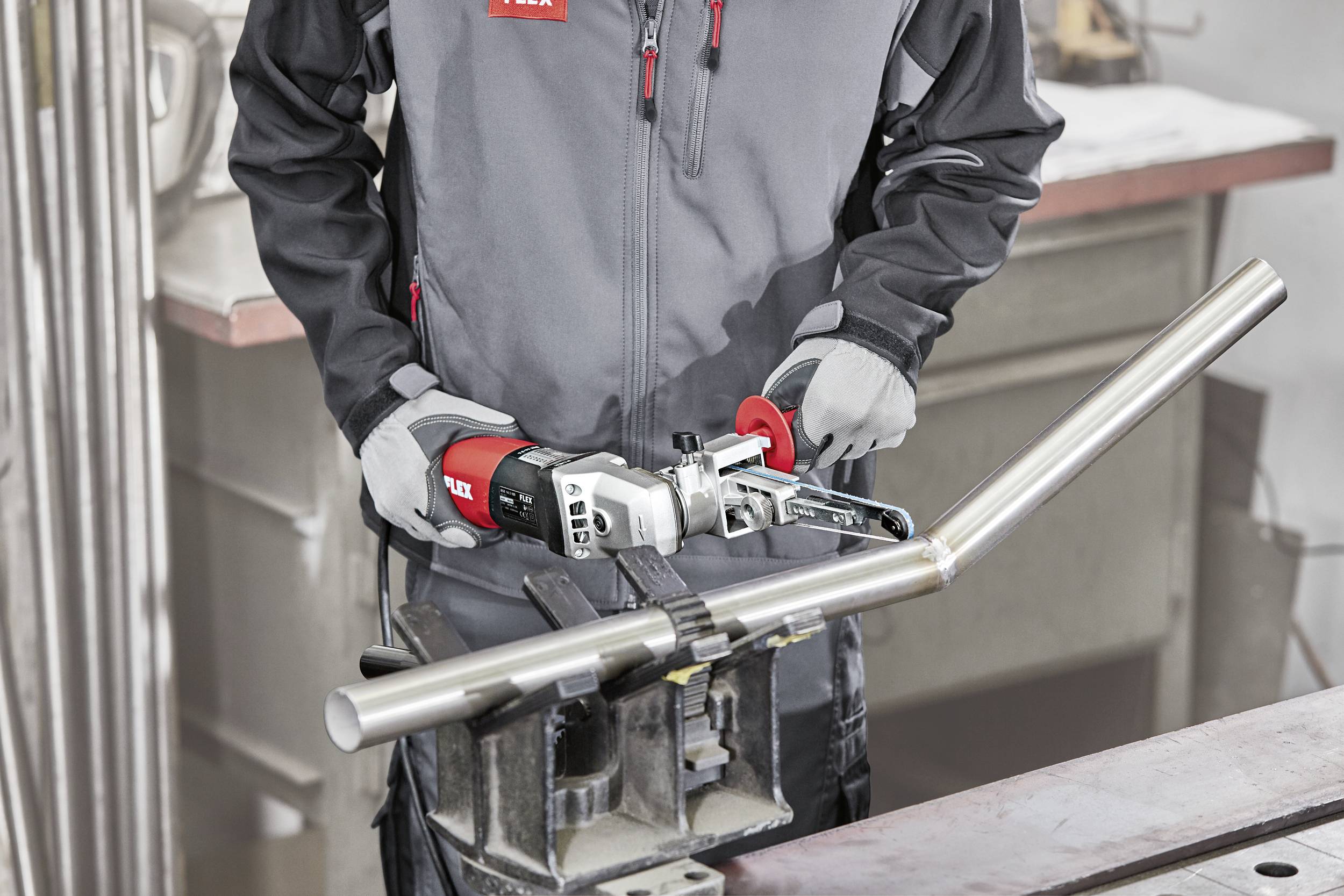 Ein Handwerker bearbeitet ein Edelstahlrohr mit einem handgeführten Werkzeug in einer Werkstatt. Das Rohr ist in einem Schraubstock eingespannt.