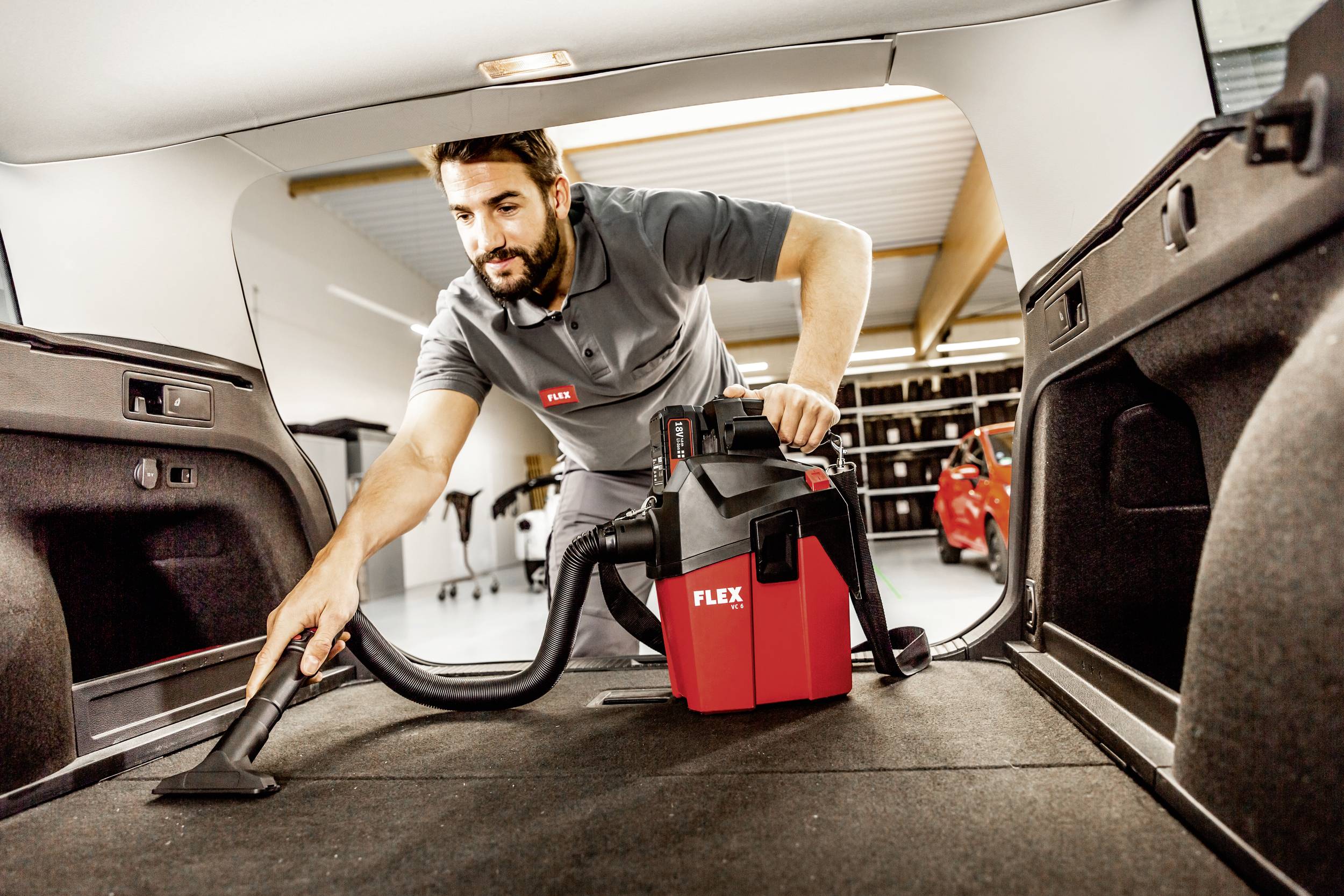 Ein Mann saugt den Kofferraum eines Autos mit einem roten FLEX-Staubsauger.