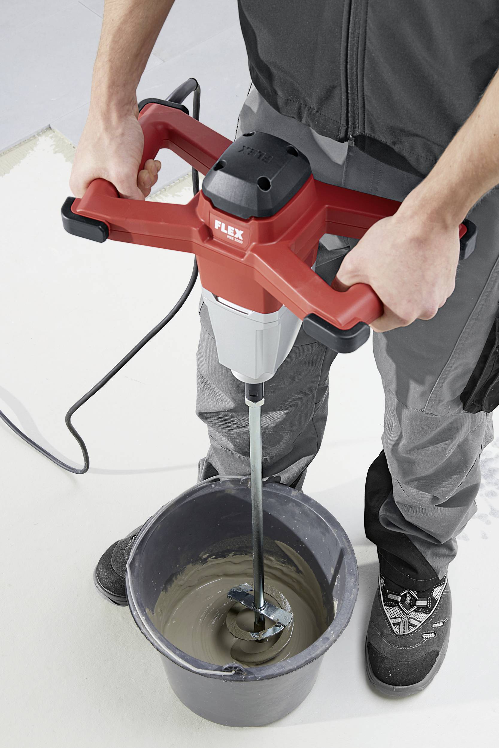 Eine Person mischt mit einem Elektromischer Zement oder eine ähnliche Mischung in einem Eimer. Der Mischer hat einen roten Griff.