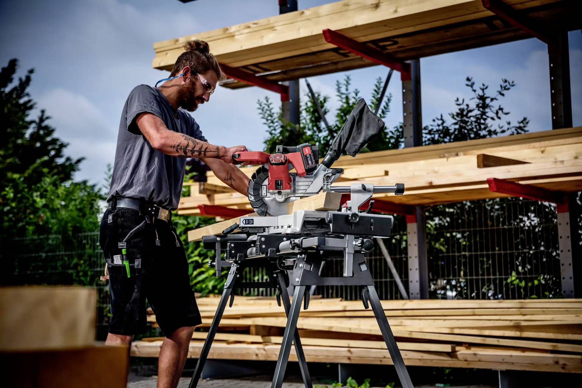 Ein Handwerker schneidet auf einer Baustelle mit einer Motorsäge Holz. Im Hintergrund sind gestapelte Holzbalken zu sehen.
