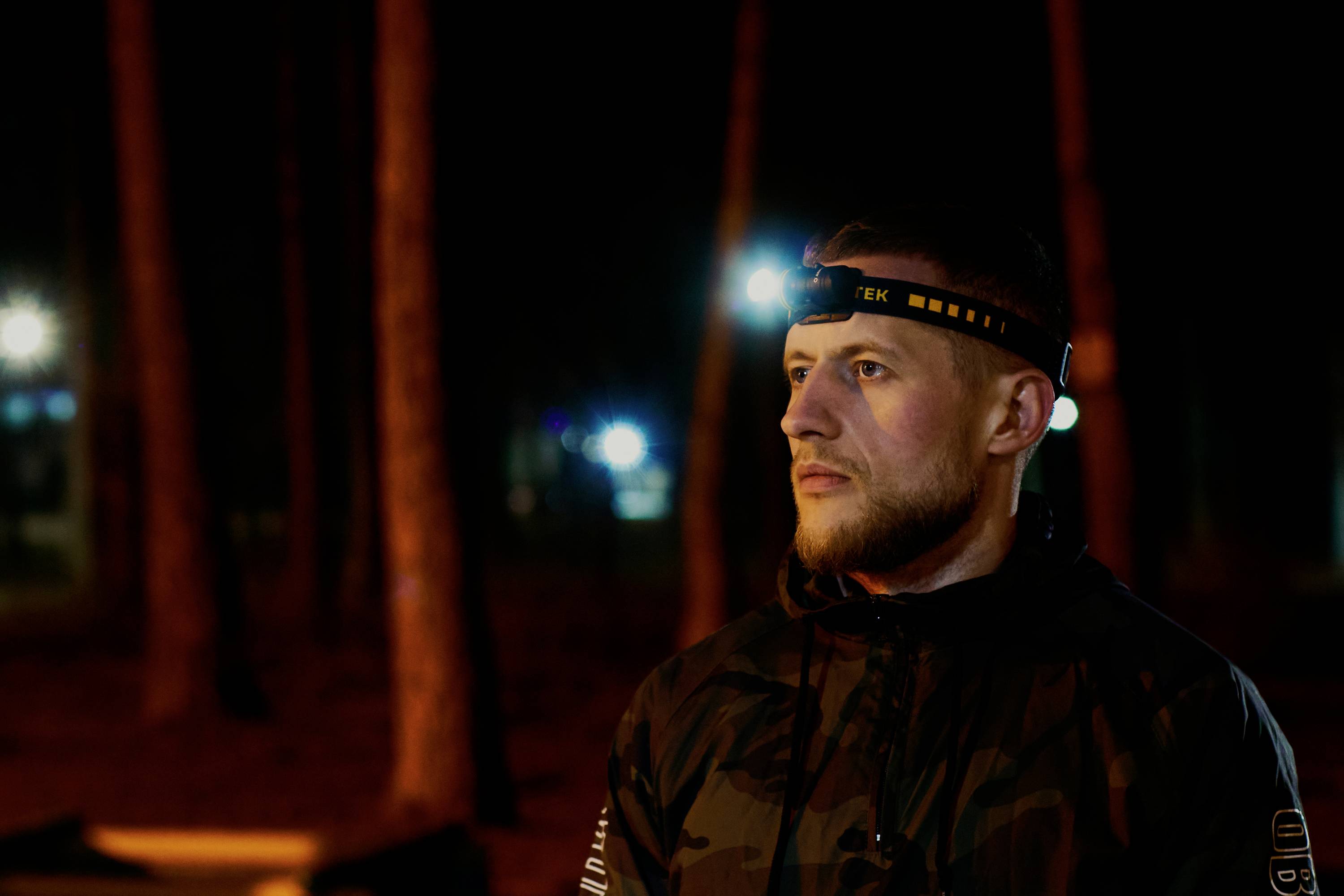 Mann bei Nacht im Wald mit Stirnlampe, schaut nachdenklich in die Ferne.