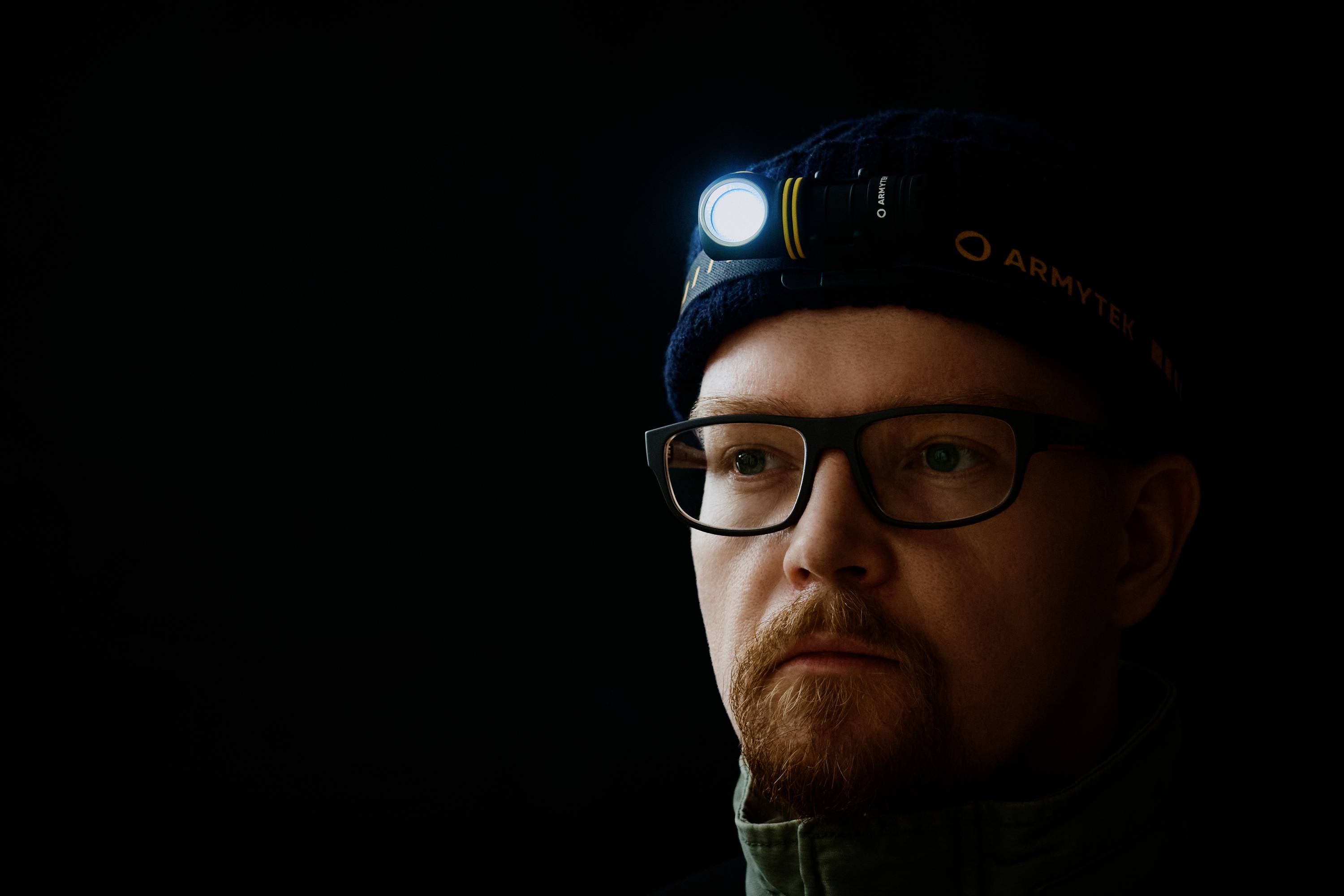 Ein Mann mit Brille trägt eine leuchtende Stirnlampe in dunkler Umgebung.
