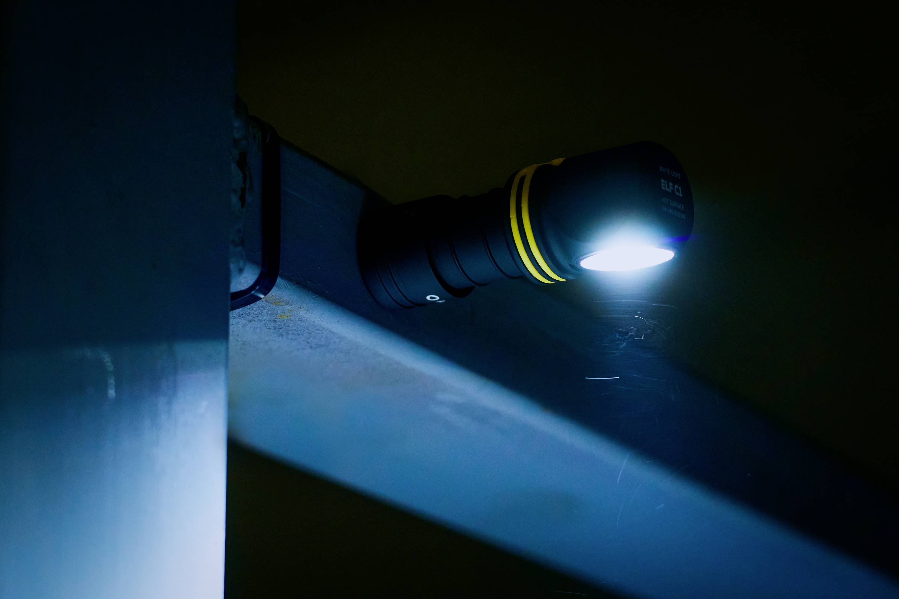 Taschenlampe mit gelben Streifen leuchtet an einer Metalloberfläche. Entspannte, dunkle Umgebung.
