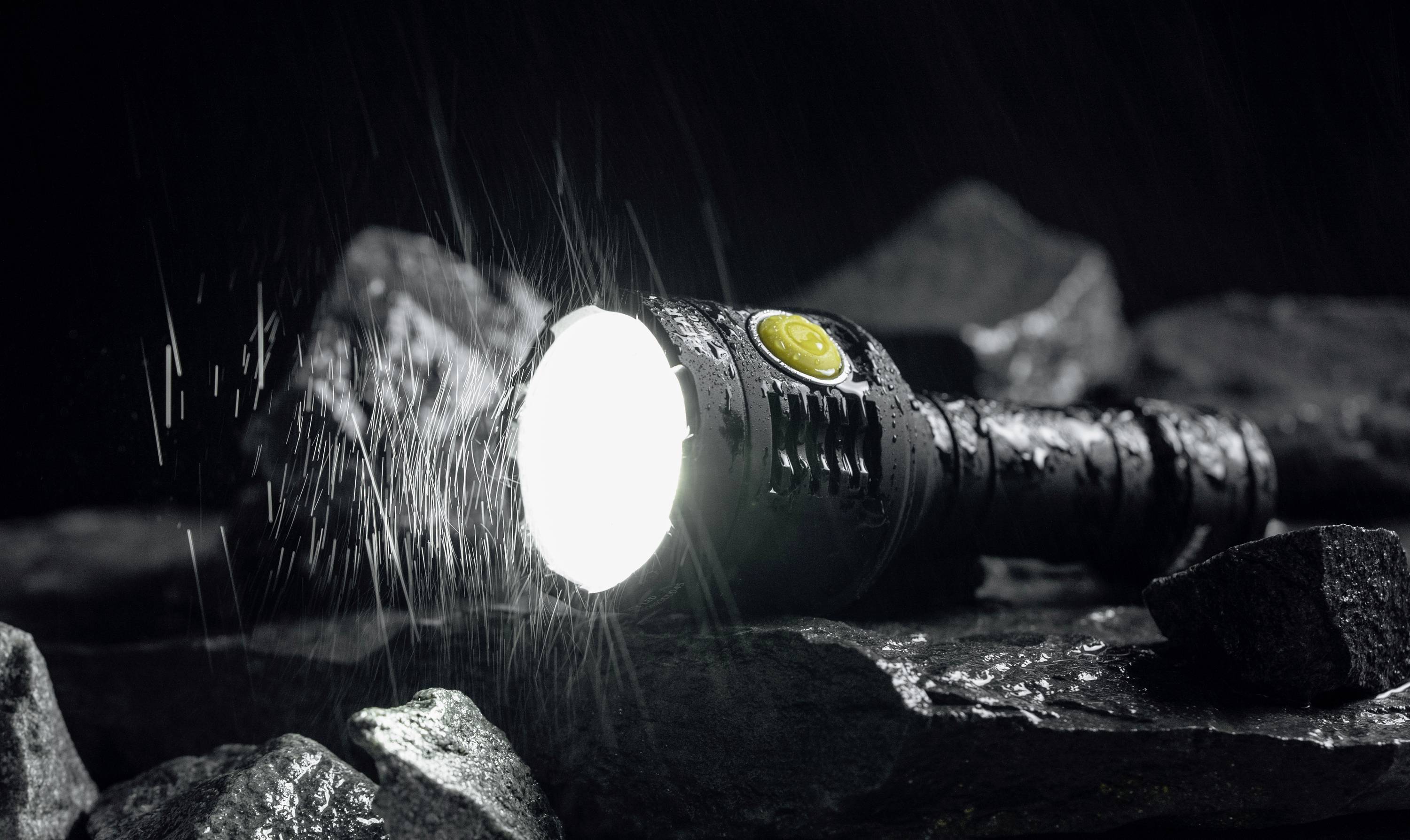 Taschenlampe leuchtet hell im Regen auf Steinen; vermittelt Robustheit und Zuverlässigkeit bei widrigen Wetterbedingungen.