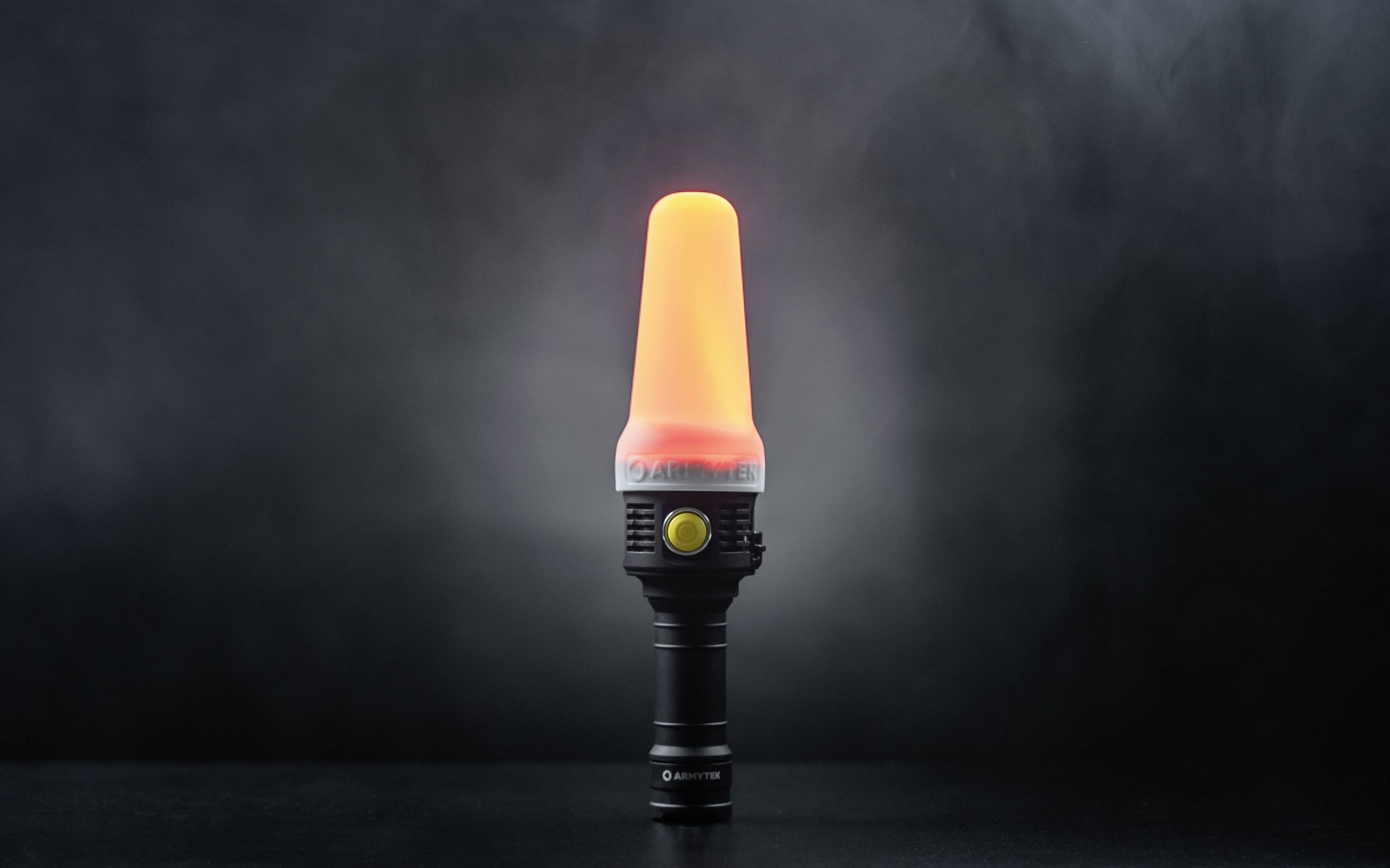 Eine Taschenlampe mit einem orangefarbenen Leuchtaufsatz leuchtet hell in einem dunklen Raum. Sie strahlt ein warmes, intensives Licht aus.