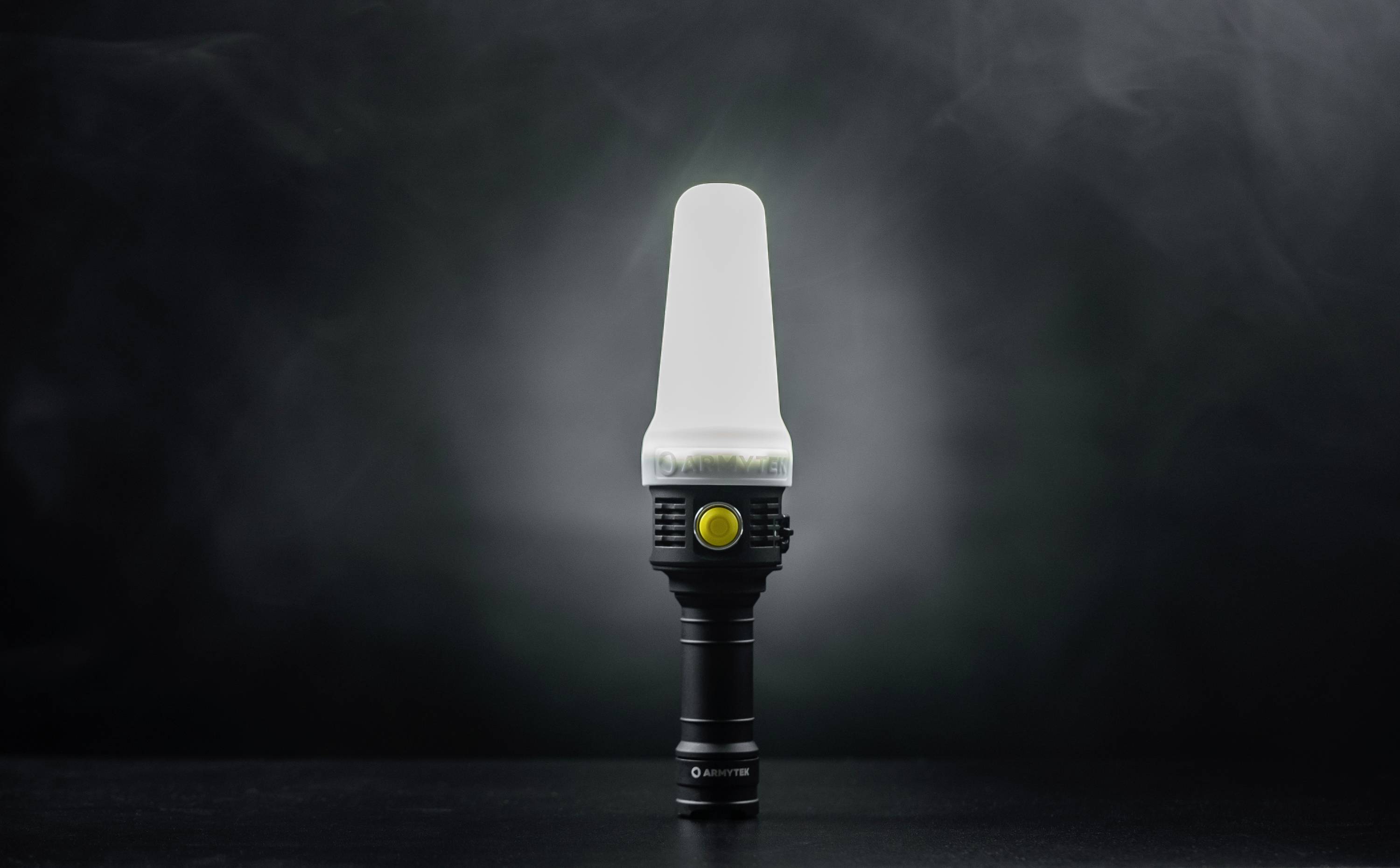 Eine Taschenlampe mit diffuser Lichtabdeckung, steht aufrecht auf einer dunklen Oberfläche. Ein gelber Knopf ist sichtbar.