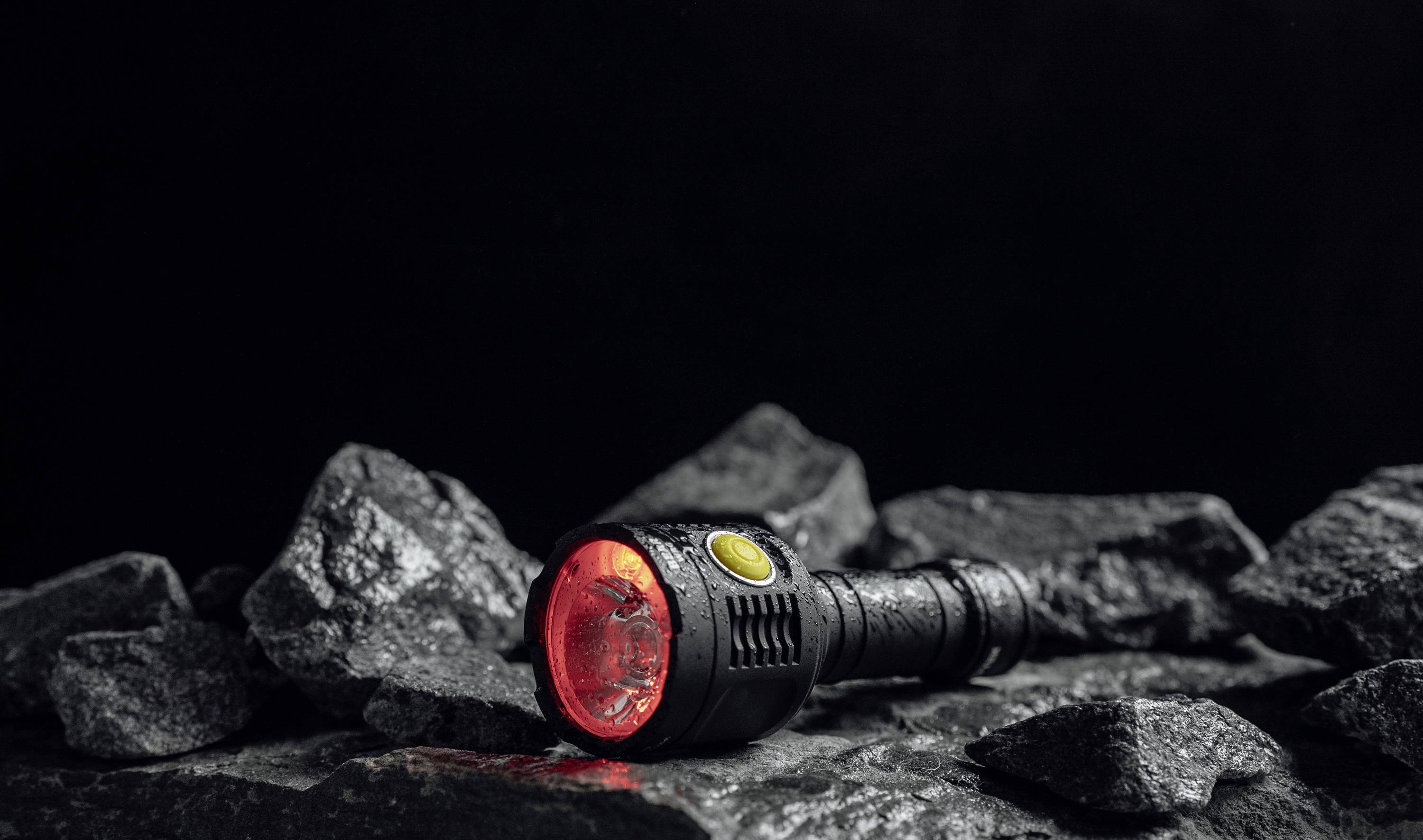 Taschenlampe mit rotem Licht, auf steiniger Oberfläche liegend, beleuchtet in einer dunklen Umgebung.