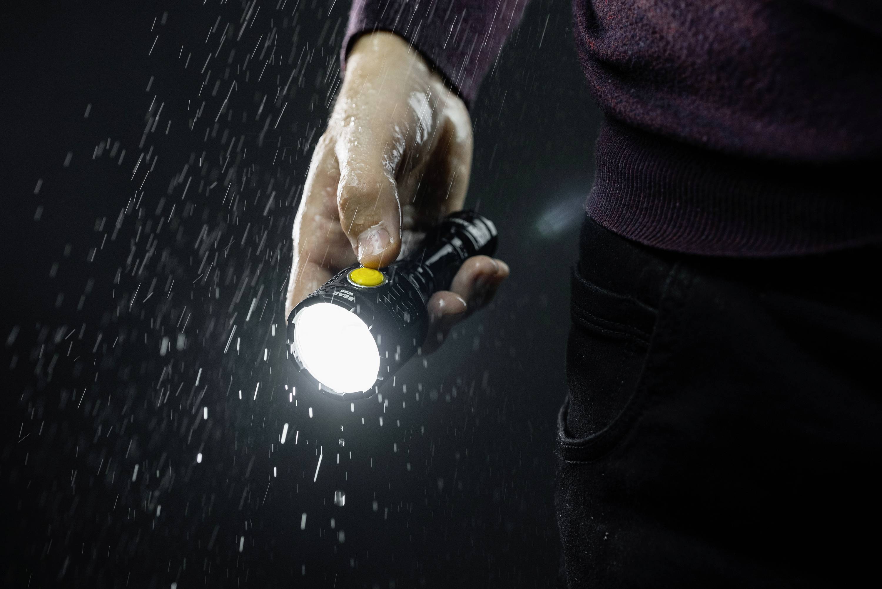 Eine Person hält eine Taschenlampe im Regen. Wasser tropft ab und strahlt helles Licht aus.