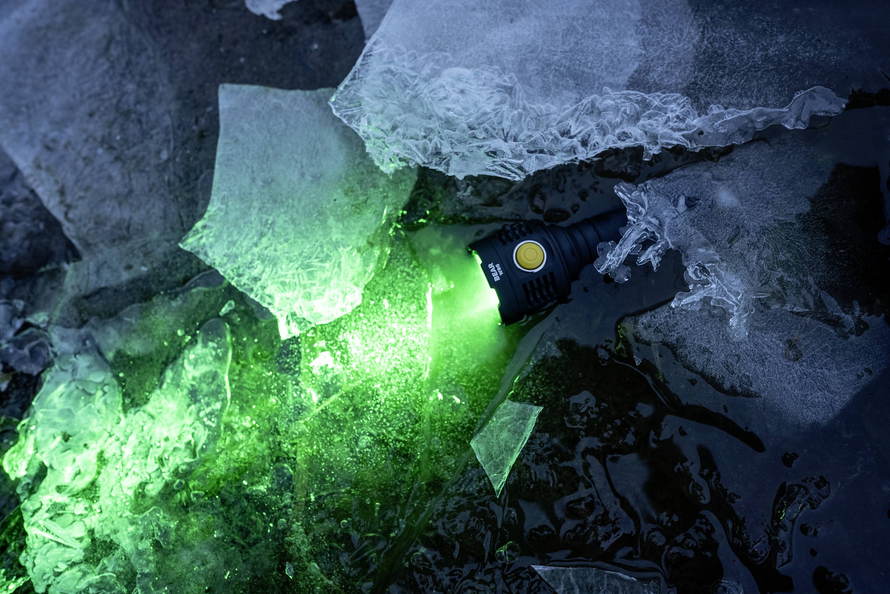 Eine leuchtende Taschenlampe mit grünem Licht liegt zwischen Eisstücken und spiegelt sich im Wasser wider.