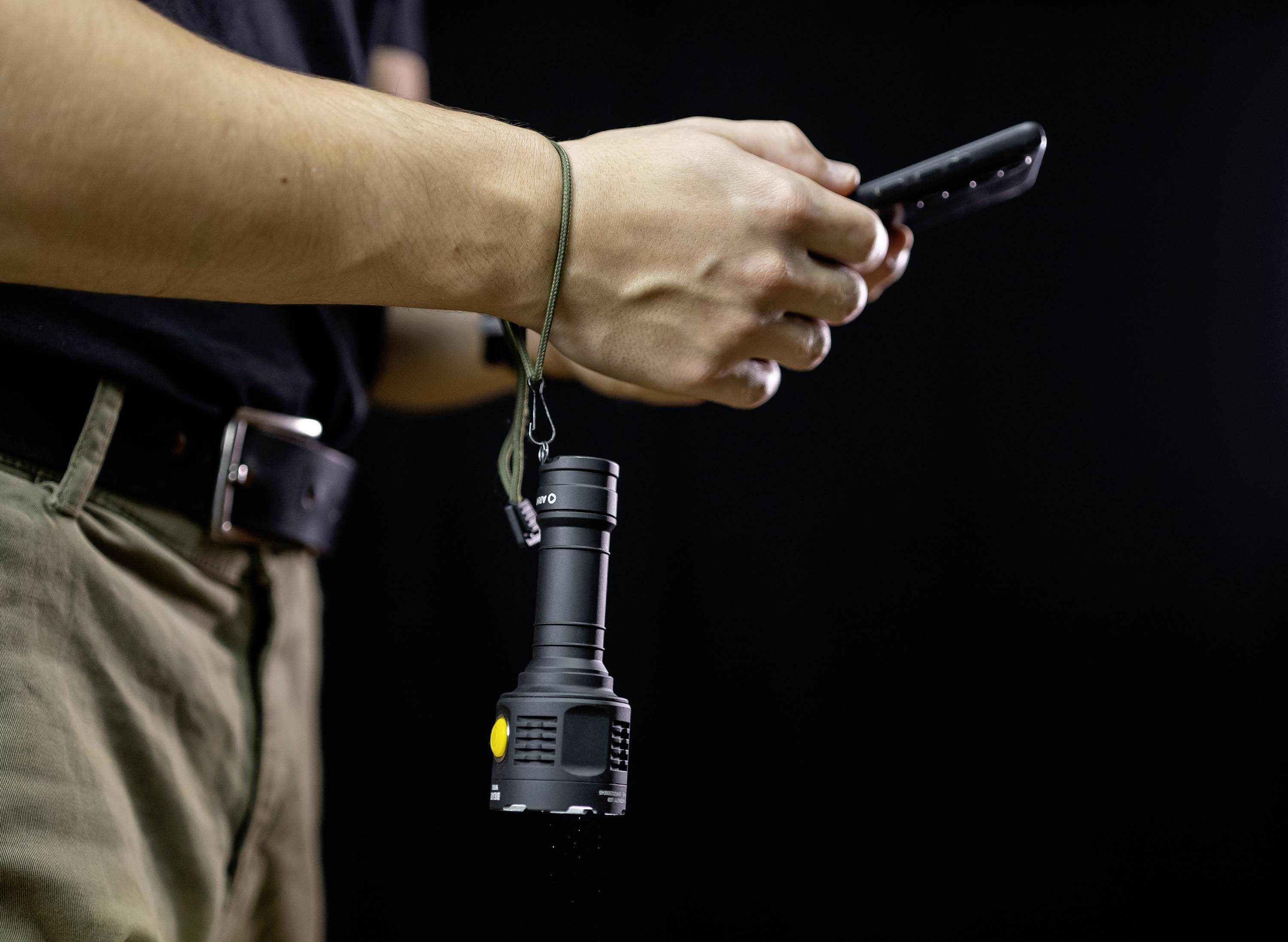 Person hält eine Taschenlampe und ein Smartphone vor einem dunklen Hintergrund, bereit für Outdoor-Aktivitäten oder Nachtarbeit.