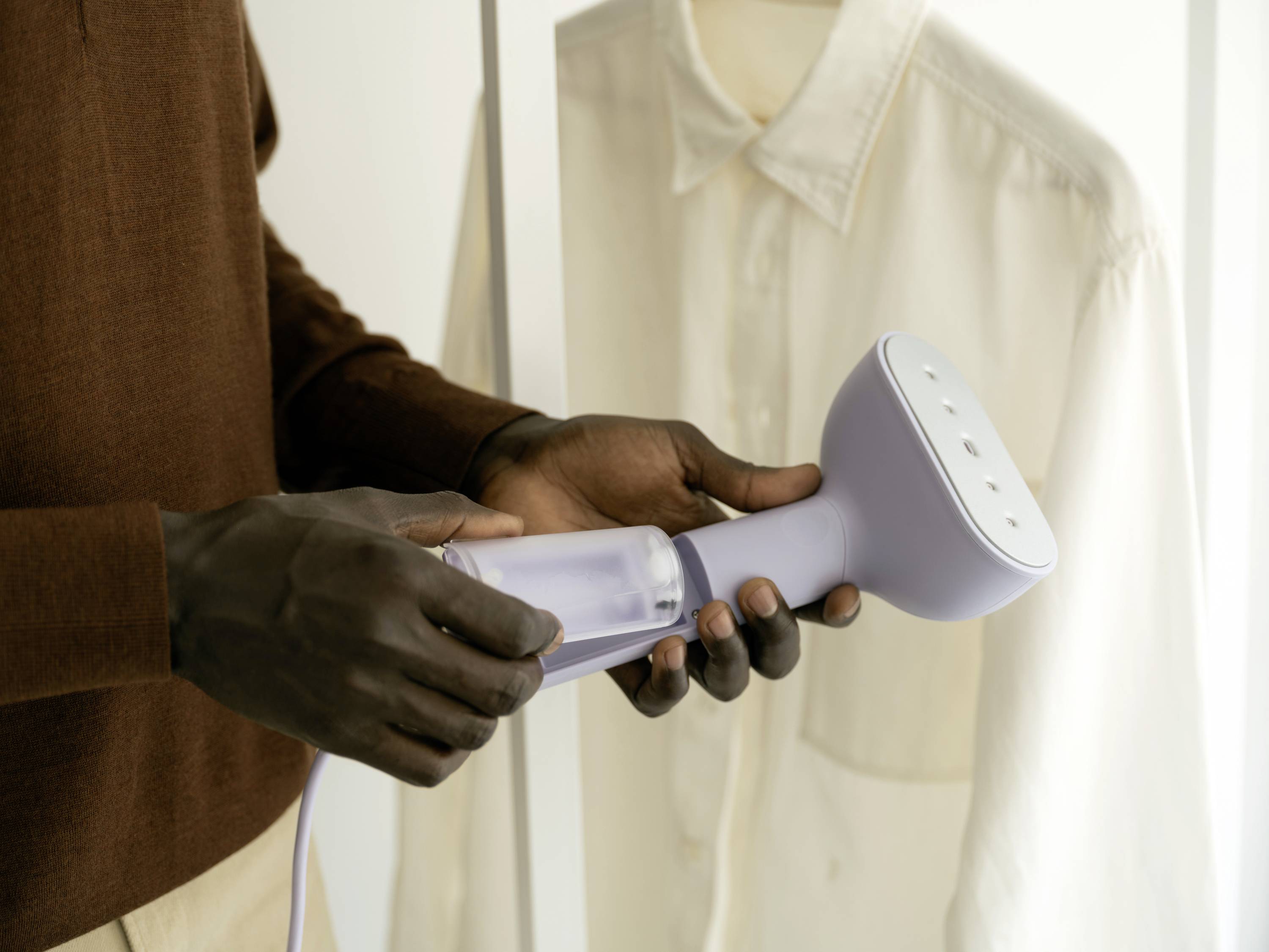 Person nutzt ein Dampfbügeleisen, um ein weißes Hemd zu glätten.