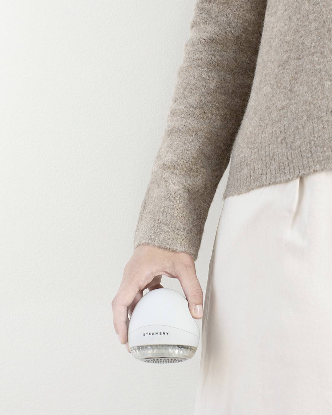 Person hält einen Stoffrasierer in der Hand, trägt ein beiges Oberteil und einen hellen Rock.