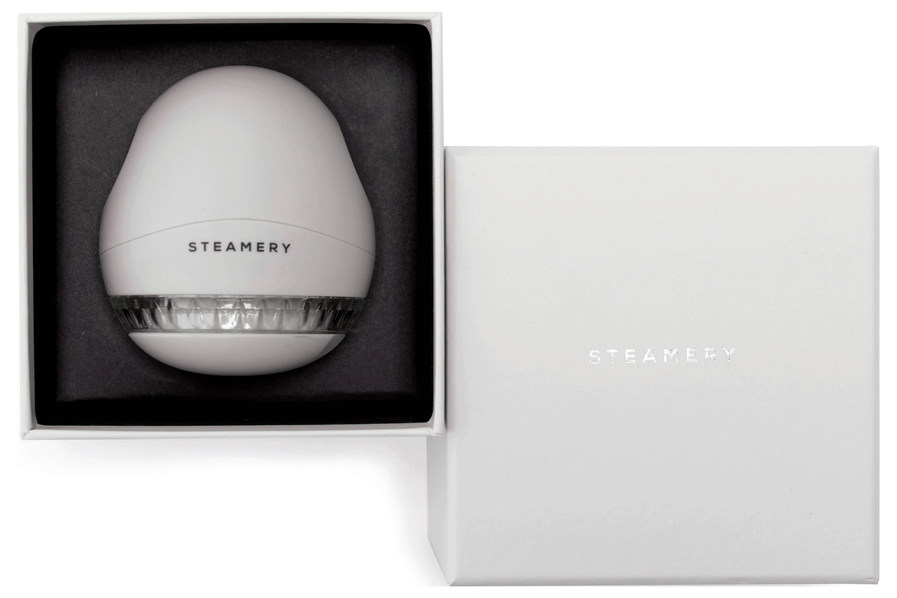 Ein Rundgerät mit der Aufschrift 'Steamery' in einer weißen Verpackung, daneben liegt eine geschlossene Box mit dem gleichen Logo.