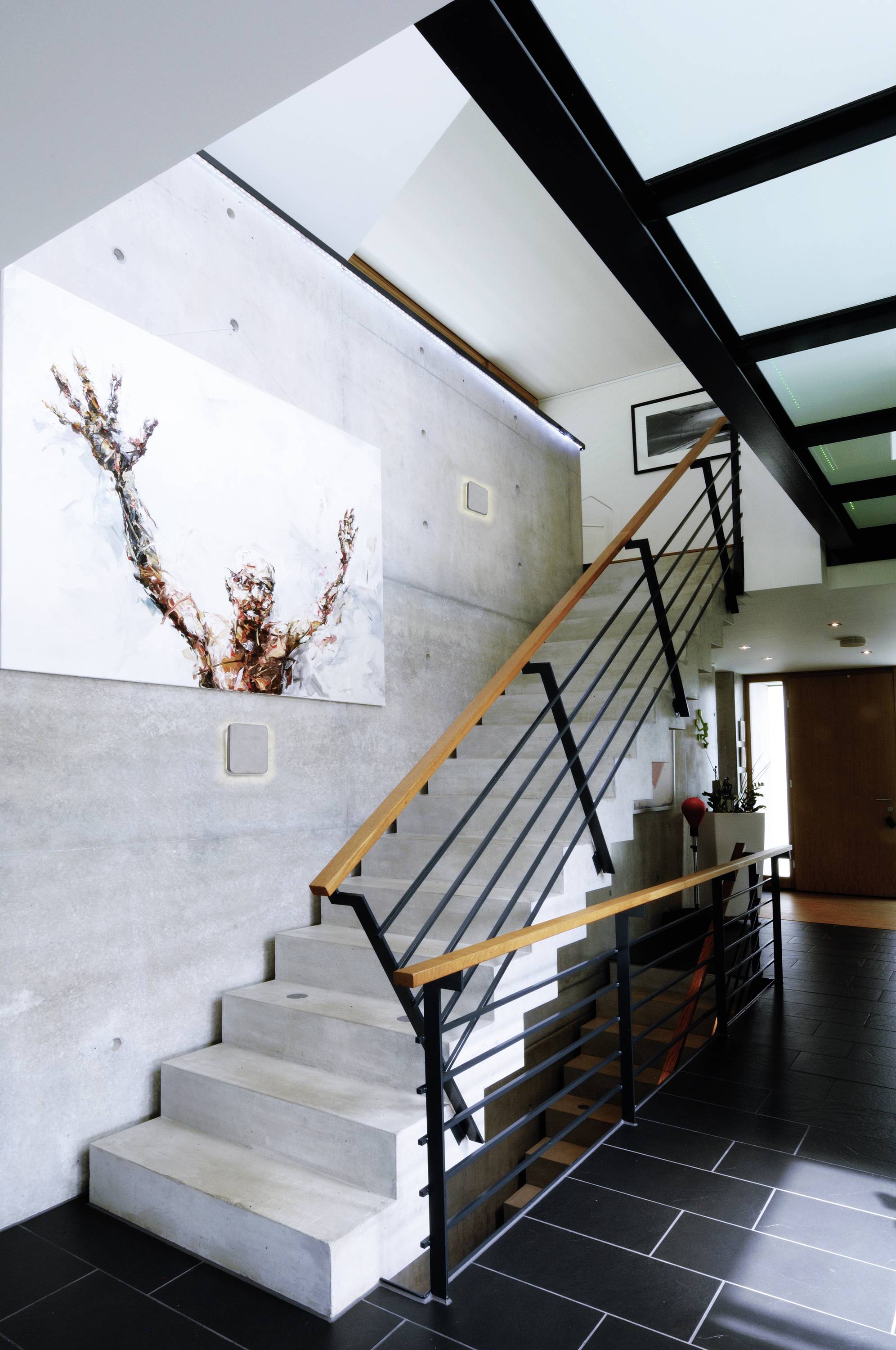 Modernes Treppenhaus mit Betonwänden, Metallgeländer und großem, abstraktem Gemälde an der Wand, das Dynamik und Bewegung zeigt.