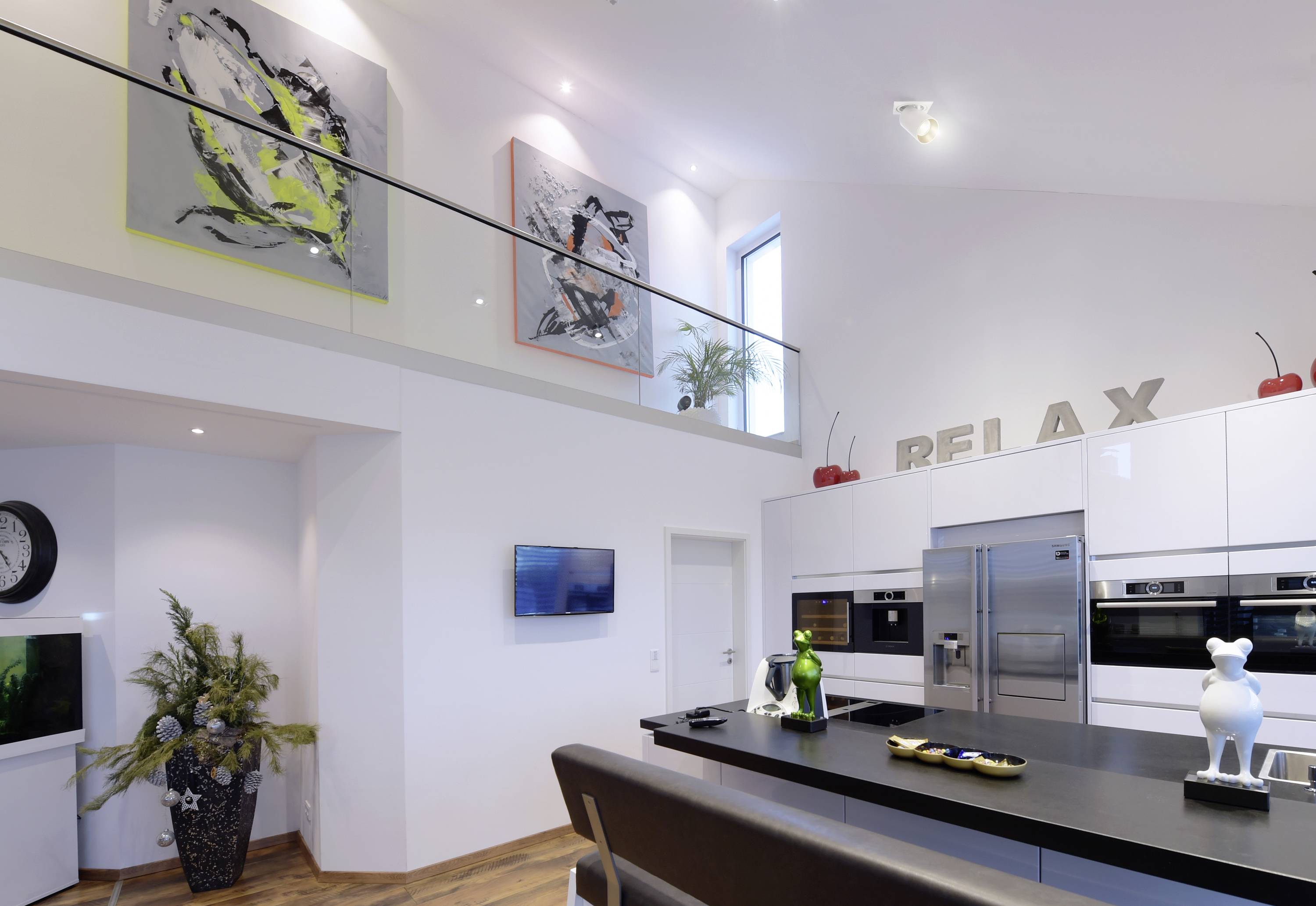 Moderne Küche mit weißer Einrichtung, Kunstwerken an der Wand und Dekorationen. Insel mit Dekor und Geräten im Vordergrund.