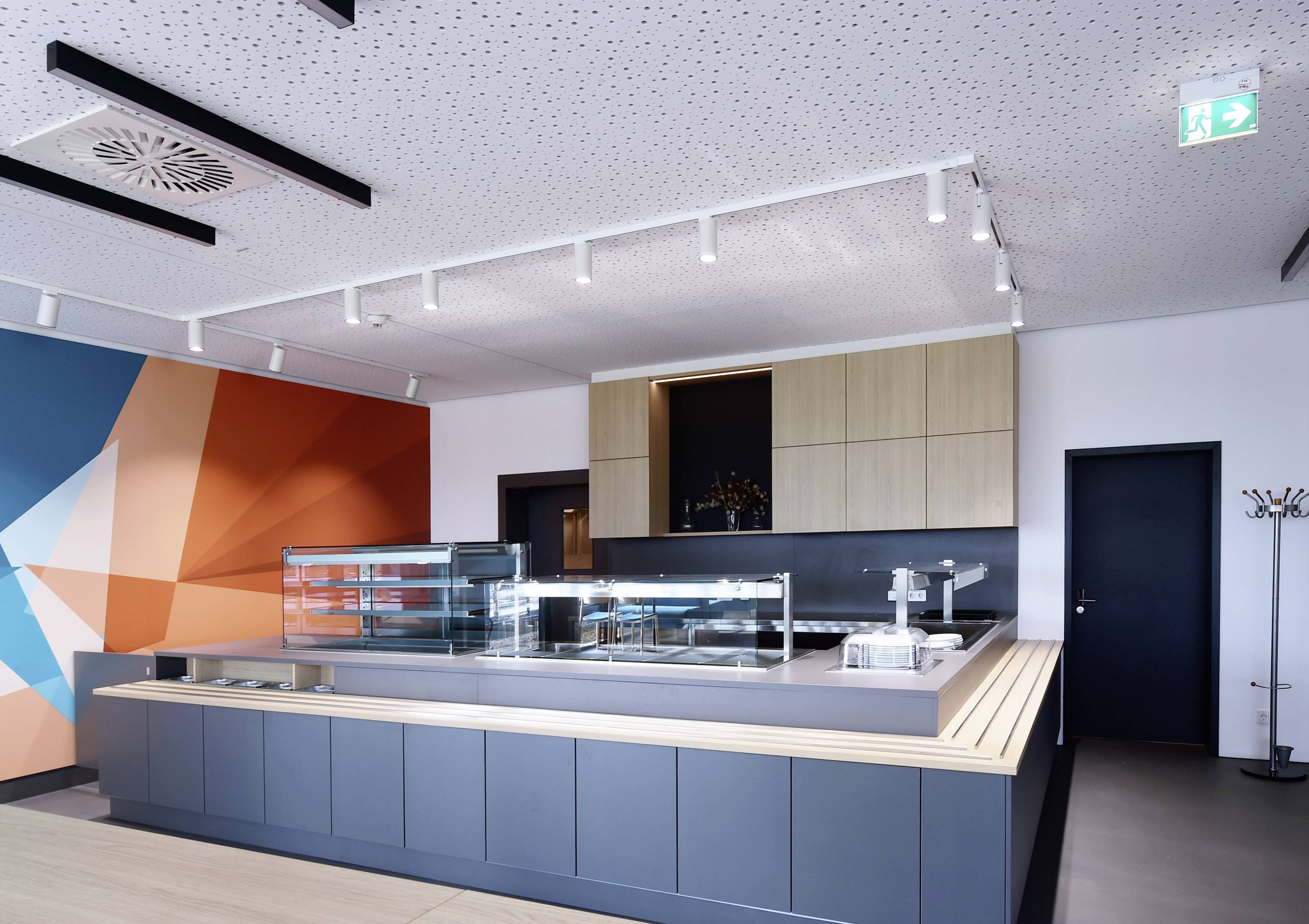 Leerer Speisesaal mit moderner Theke, blauer und orangefarbener Wandkunst, Holzdecken und Beleuchtung, ohne Personen.