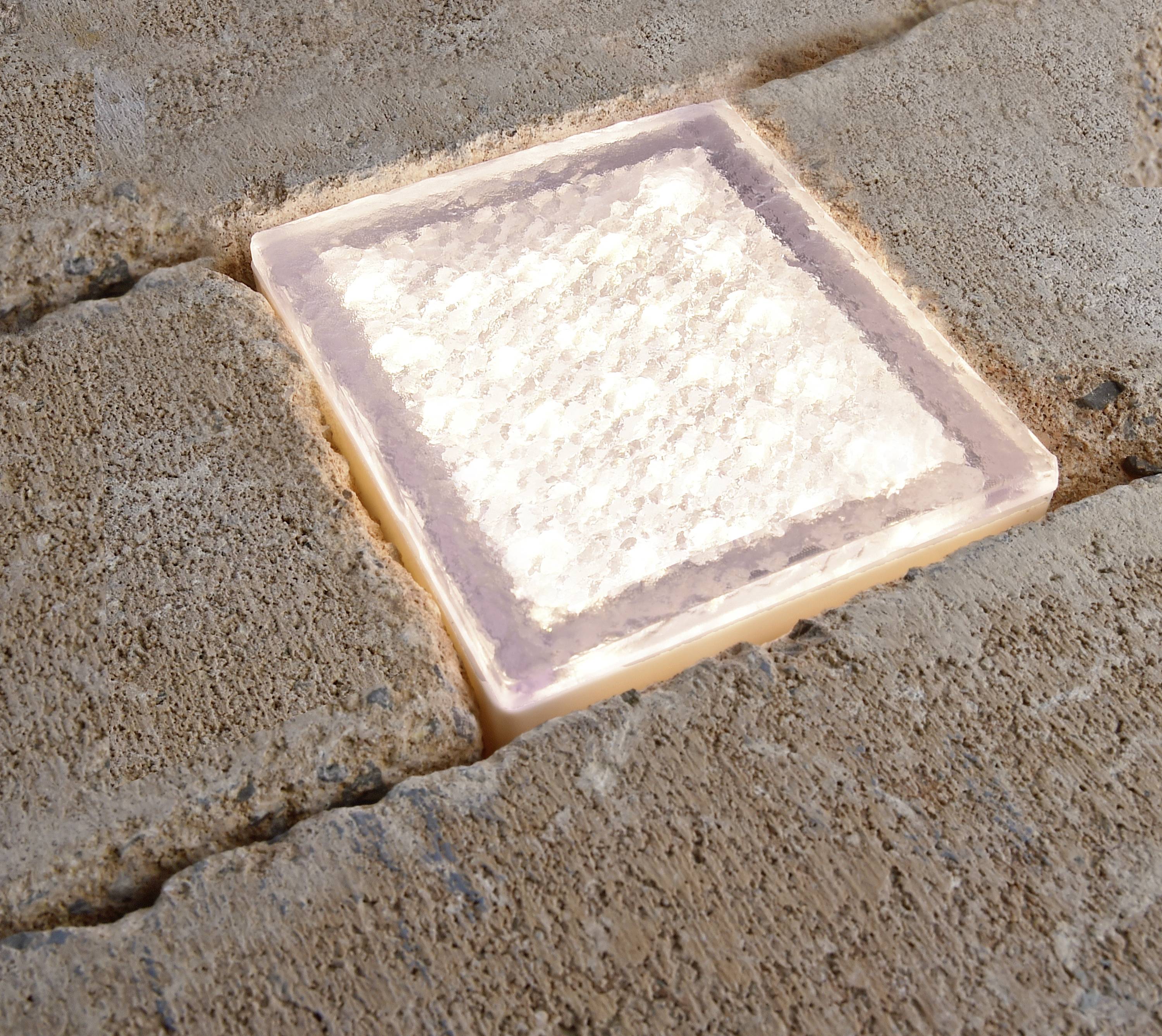 Ein leuchtender LED-Bodenstein ist in einen gepflasterten Weg integriert und erhellt die Umgebung subtil.