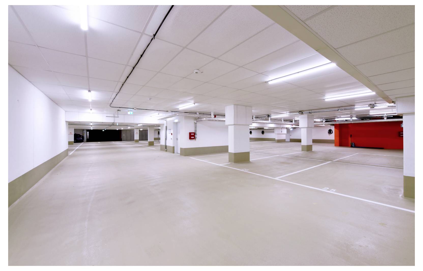 Leere Tiefgarage mit markierten Stellplätzen, weißen Säulen und einer roten Wand am hinteren Ende.