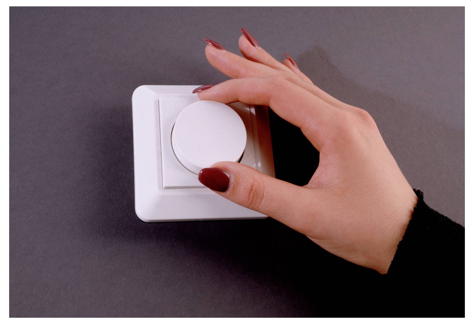 Hand, die einen weißen Wand-Dimmerschalter auf einer grauen Oberfläche dreht und so die Lichtstärke einstellt