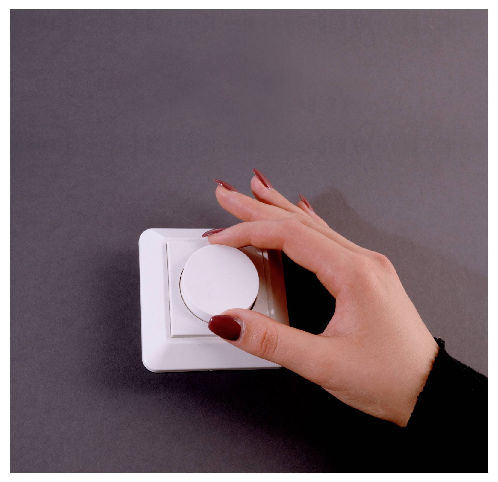 Hand dreht einen weißen Wand-Dimmer auf dunklem Hintergrund.