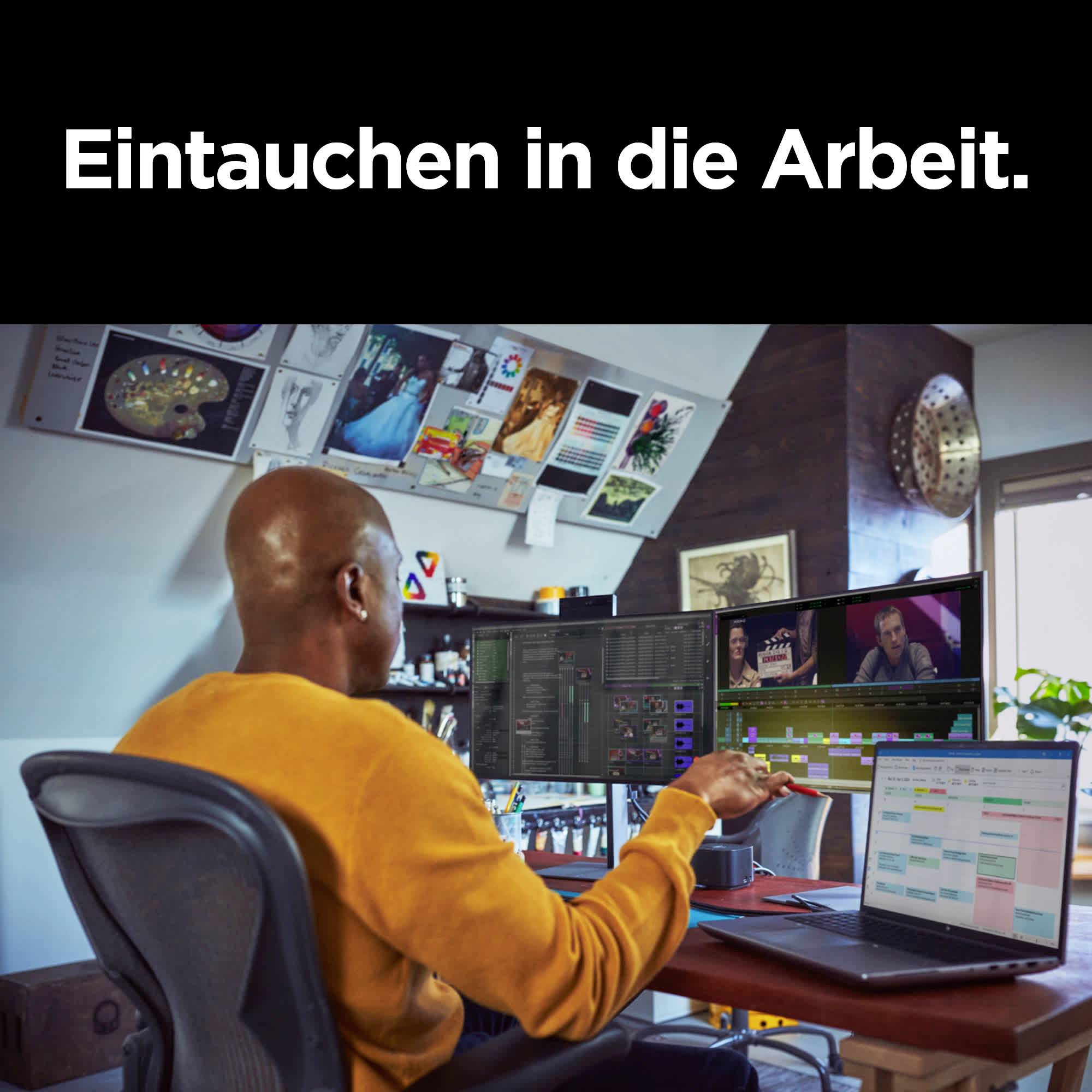 Mann in gelbem Pullover arbeitet an drei Bildschirmen. Oben steht 'Eintauchen in die Arbeit.' Büro mit dekorativen Kunstwerken.