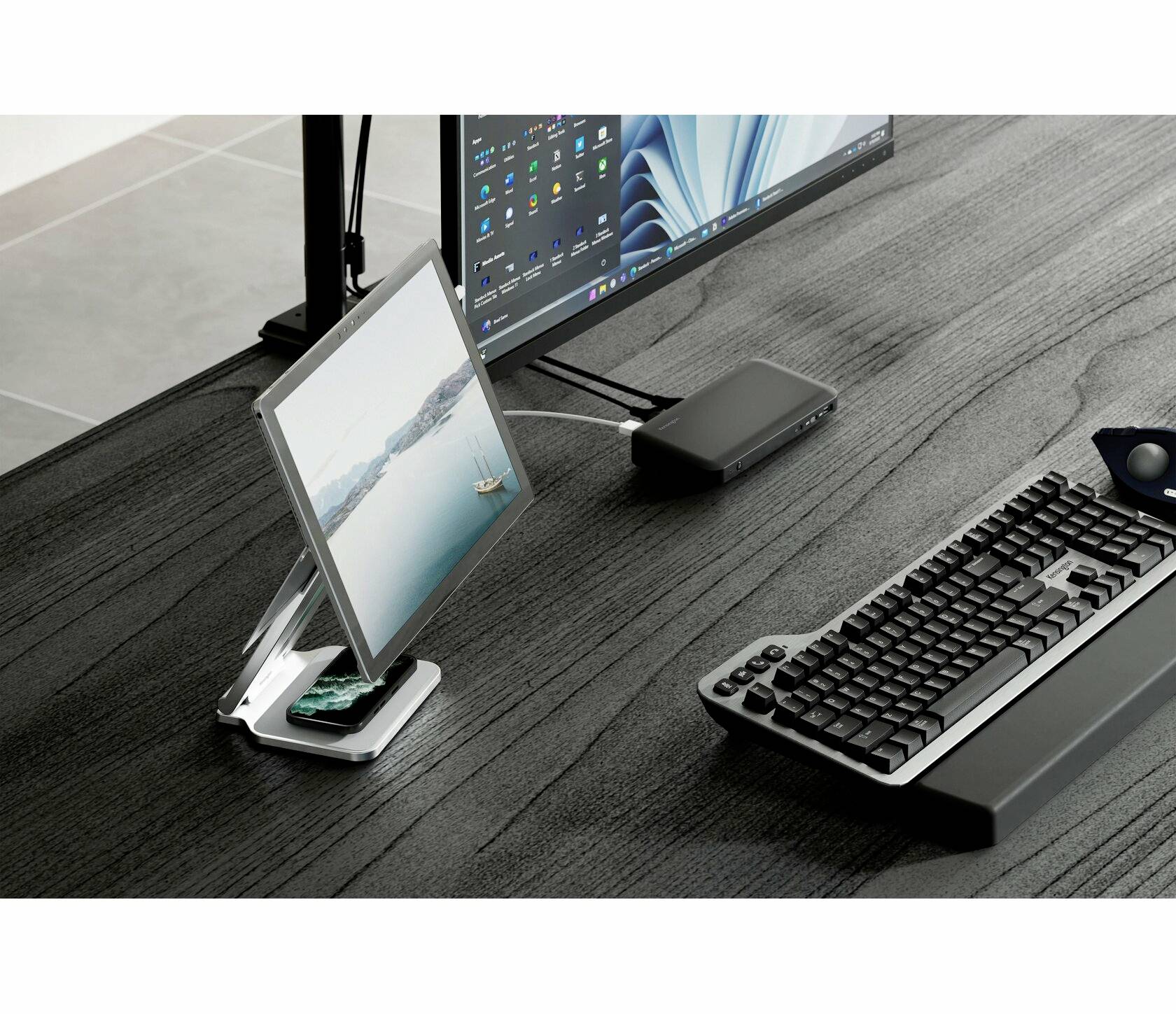 Ein moderner Schreibtisch mit einem großen Monitor, einer Tastatur und einer Halterung mit einem schräg aufgestellten Tablet.