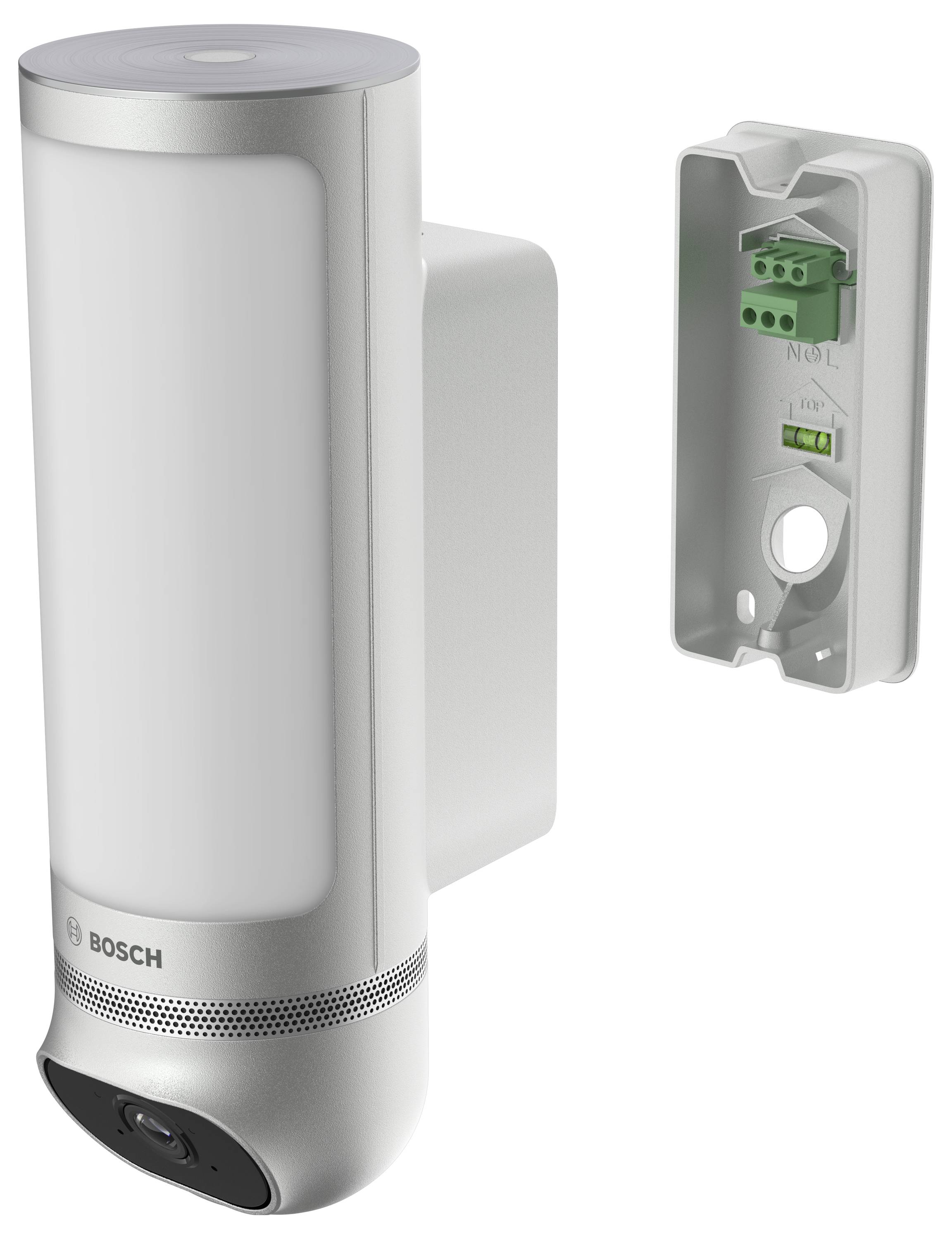 Silberne Überwachungskamera mit Wandhalterung. Rechte Seite zeigt Anschlussfeld, linke Seite Hauptkamera mit Logo.