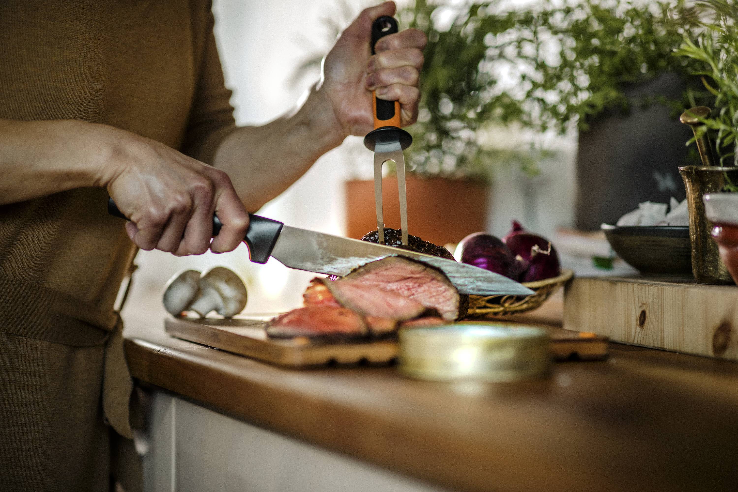 Eine Person schneidet auf einem Küchentresen Lachs. Im Hintergrund sind Pilze und ein Messerblock zu sehen. Es herrscht eine häusliche Atmosphäre.