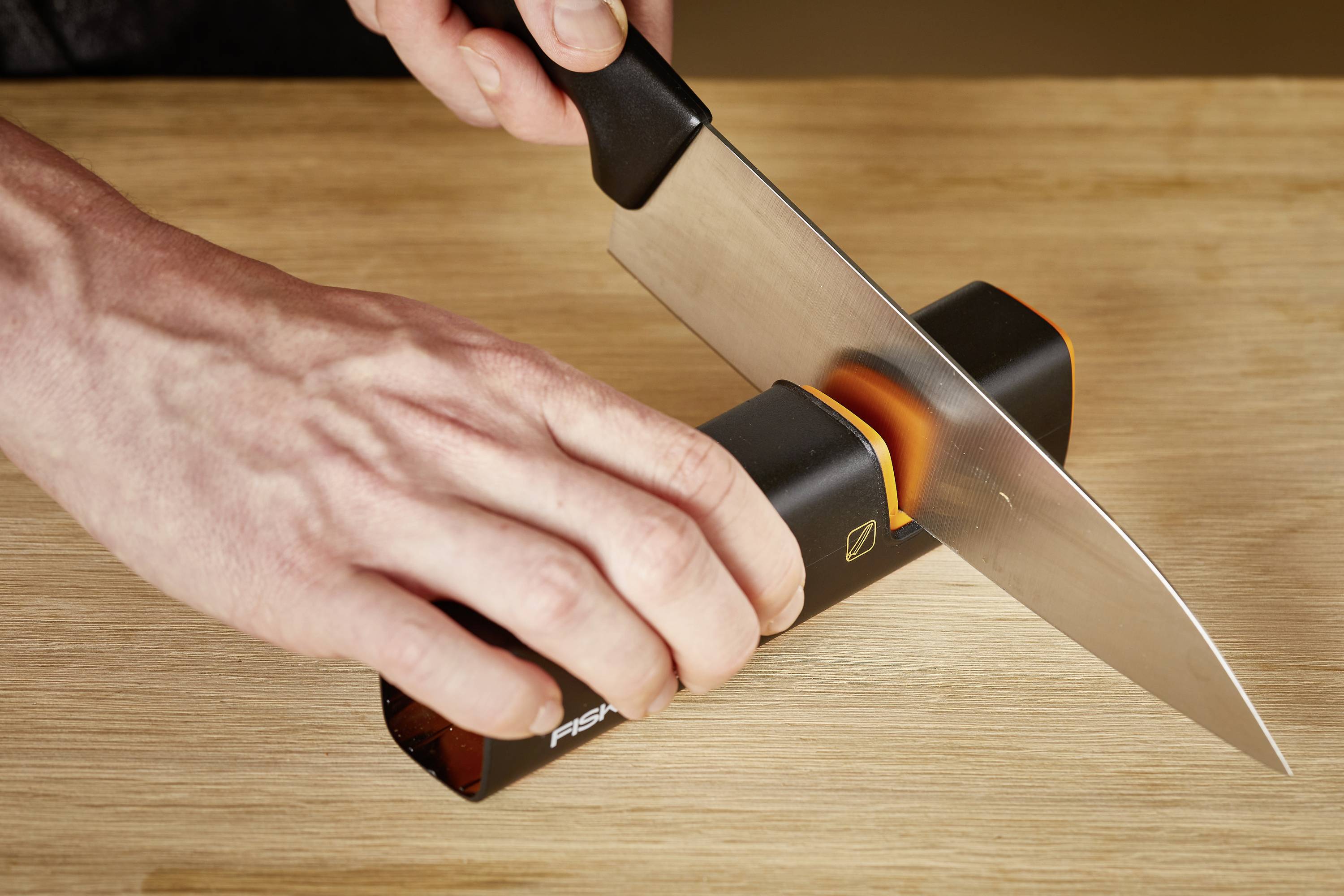 Eine Person schärft ein Küchenmesser mit einem Messerschärfer auf einer Holzoberfläche.