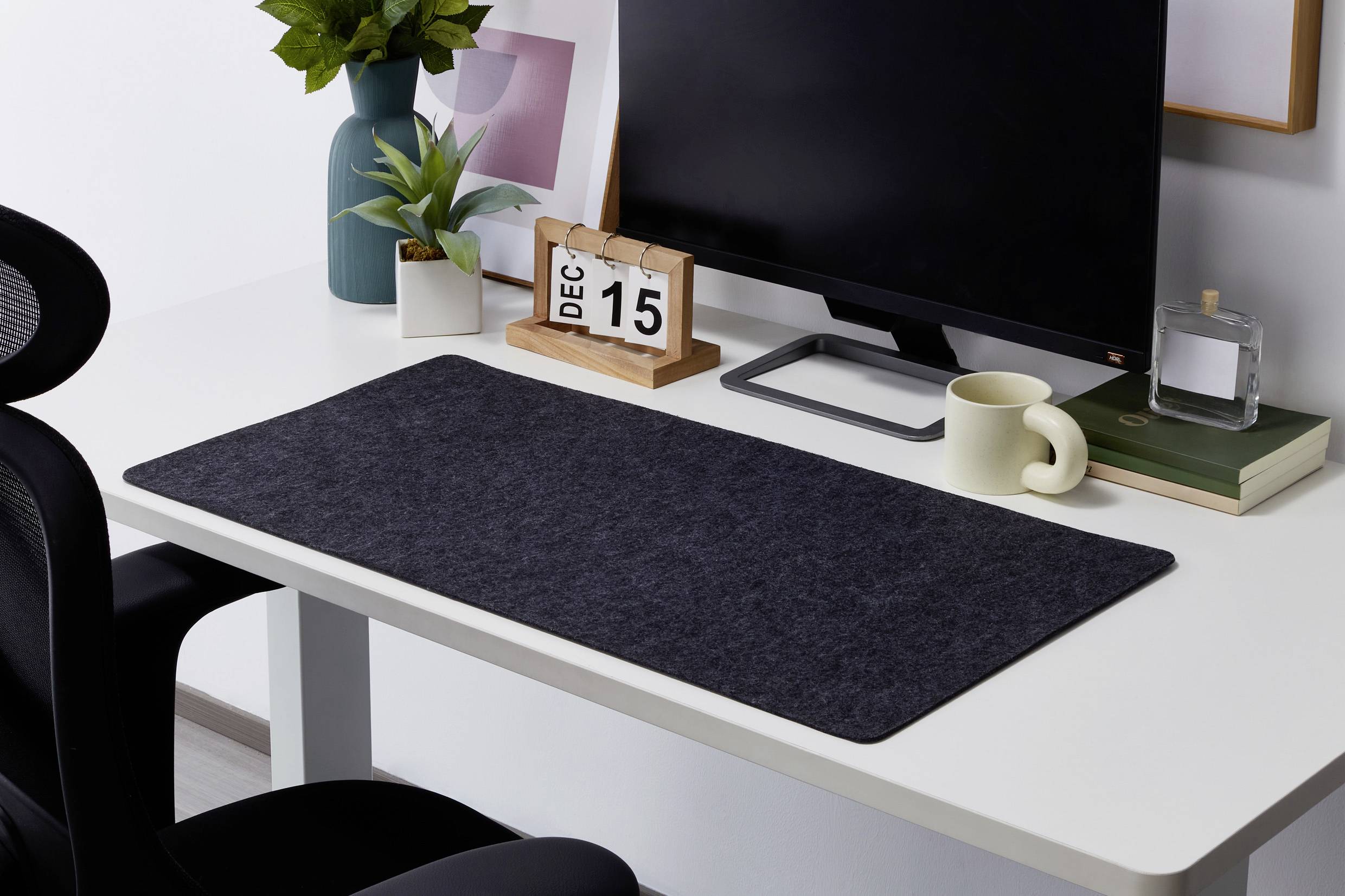 Ein aufgeräumter Schreibtisch mit einem Computer, Kalender zeigt 'DEC 15', Pflanzen, Tasse und Büchern.