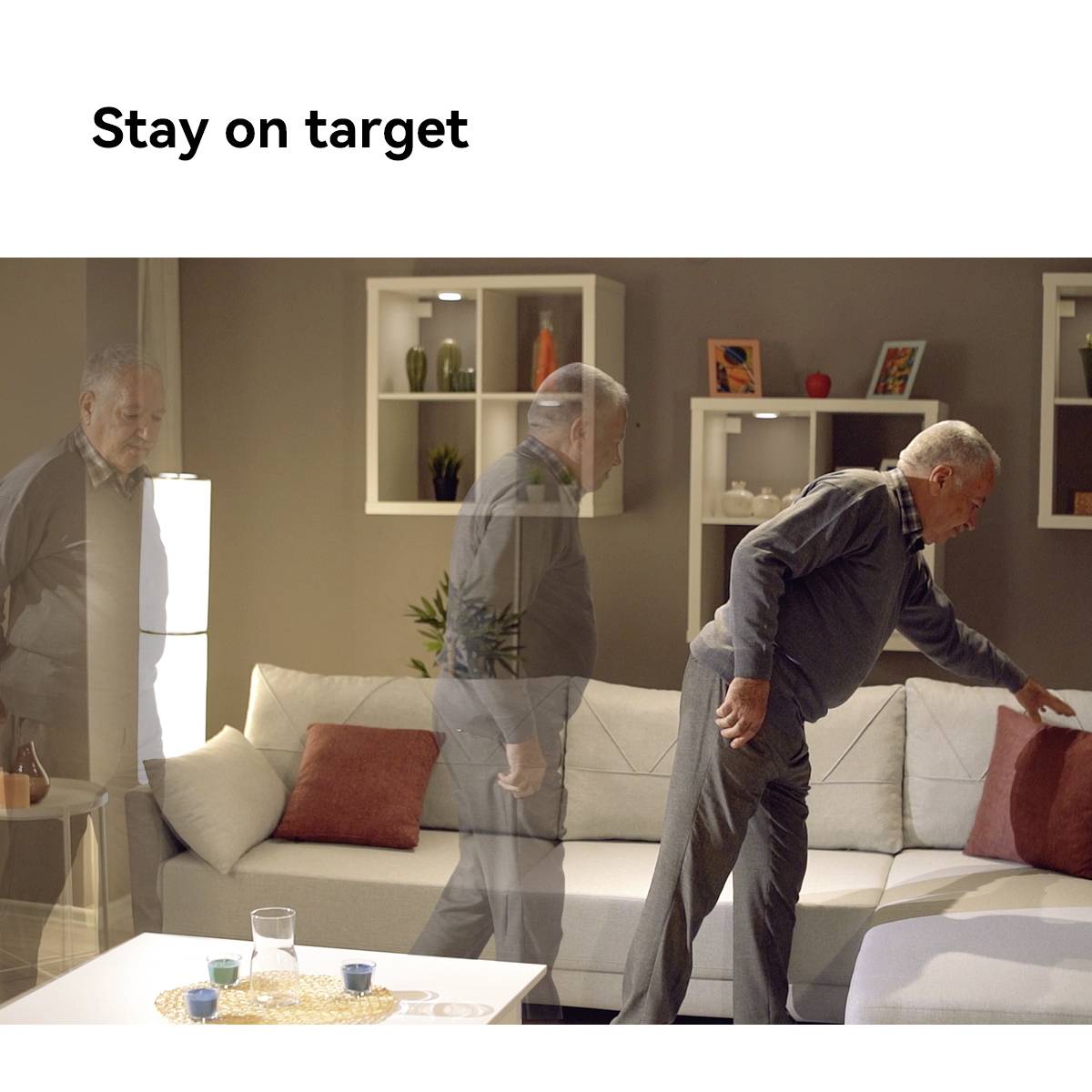 Ein älterer Mann im Wohnzimmer beugt sich zum Sofa, während sein transparentes Spiegelbild im Vordergrund steht. Auf dem Tisch zwei bunte Gläser.