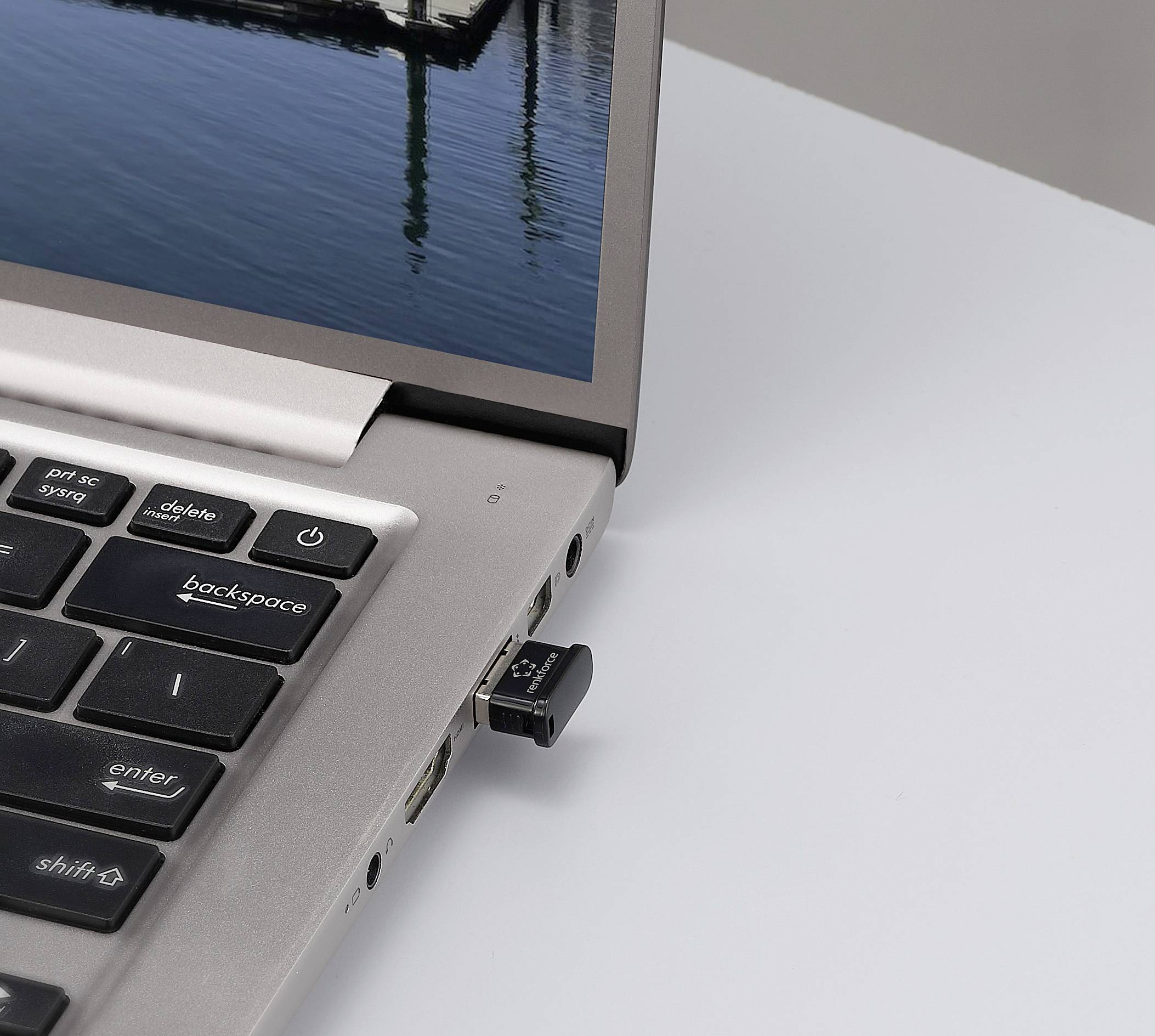 Ein silberner Laptop auf einem weißen Tisch mit einem USB-Stick im Anschluss und einem Wasser- und Brückenbild auf dem Bildschirm.